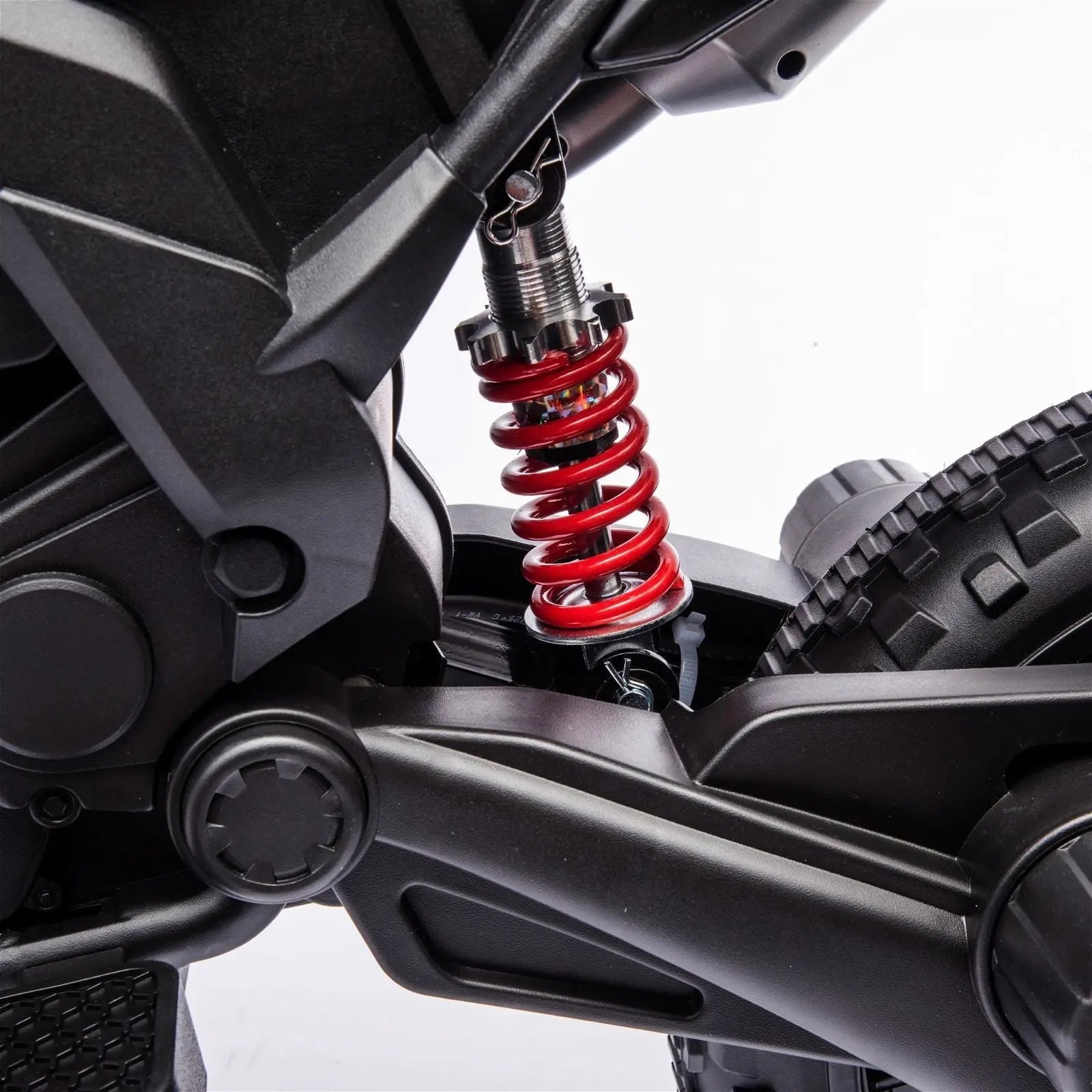 Close-up of red suspension spring on kids ride-on motorcycle, black frame and rear tire visible.