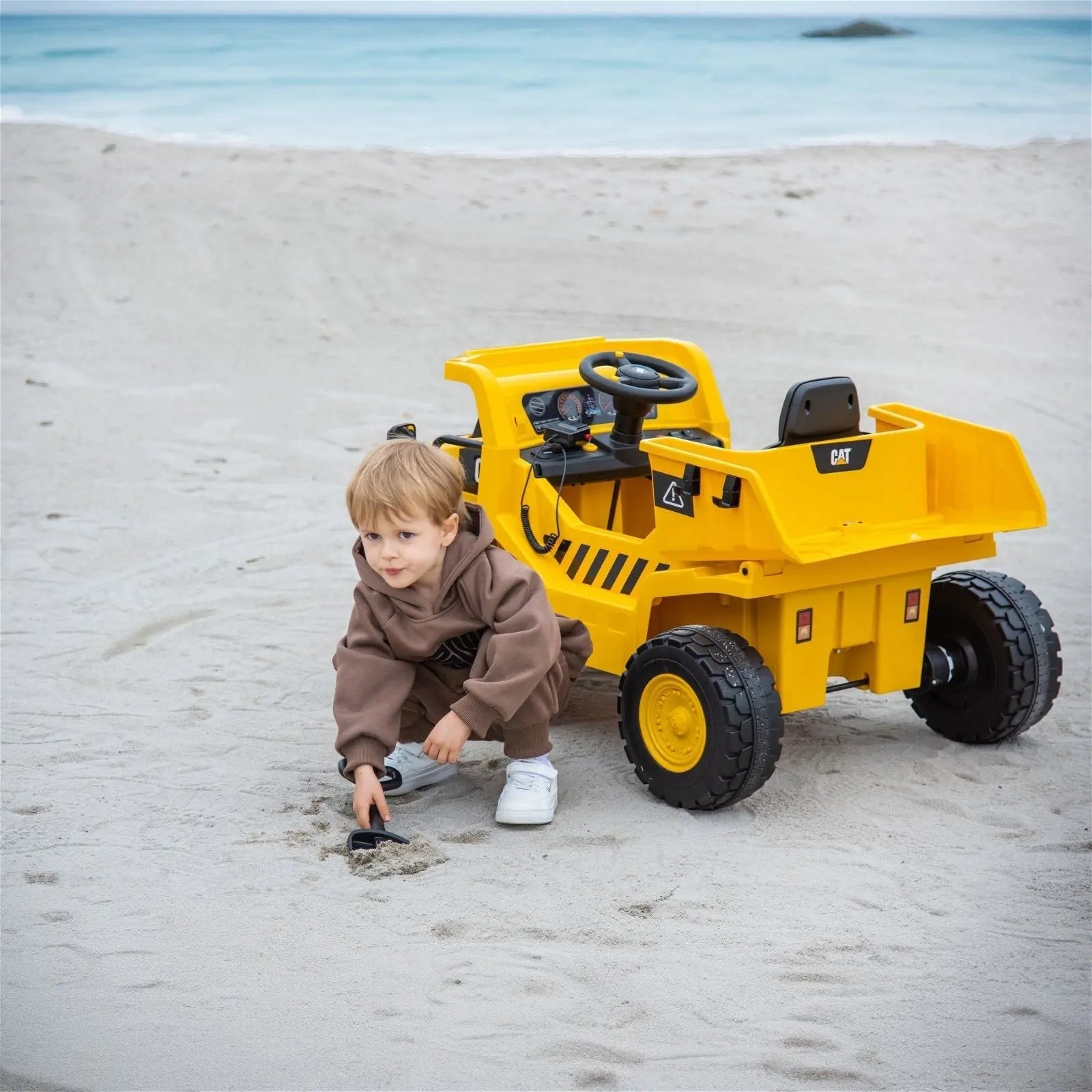 Child playing in sand beside yellow electric ride-on dump truck toy on beach