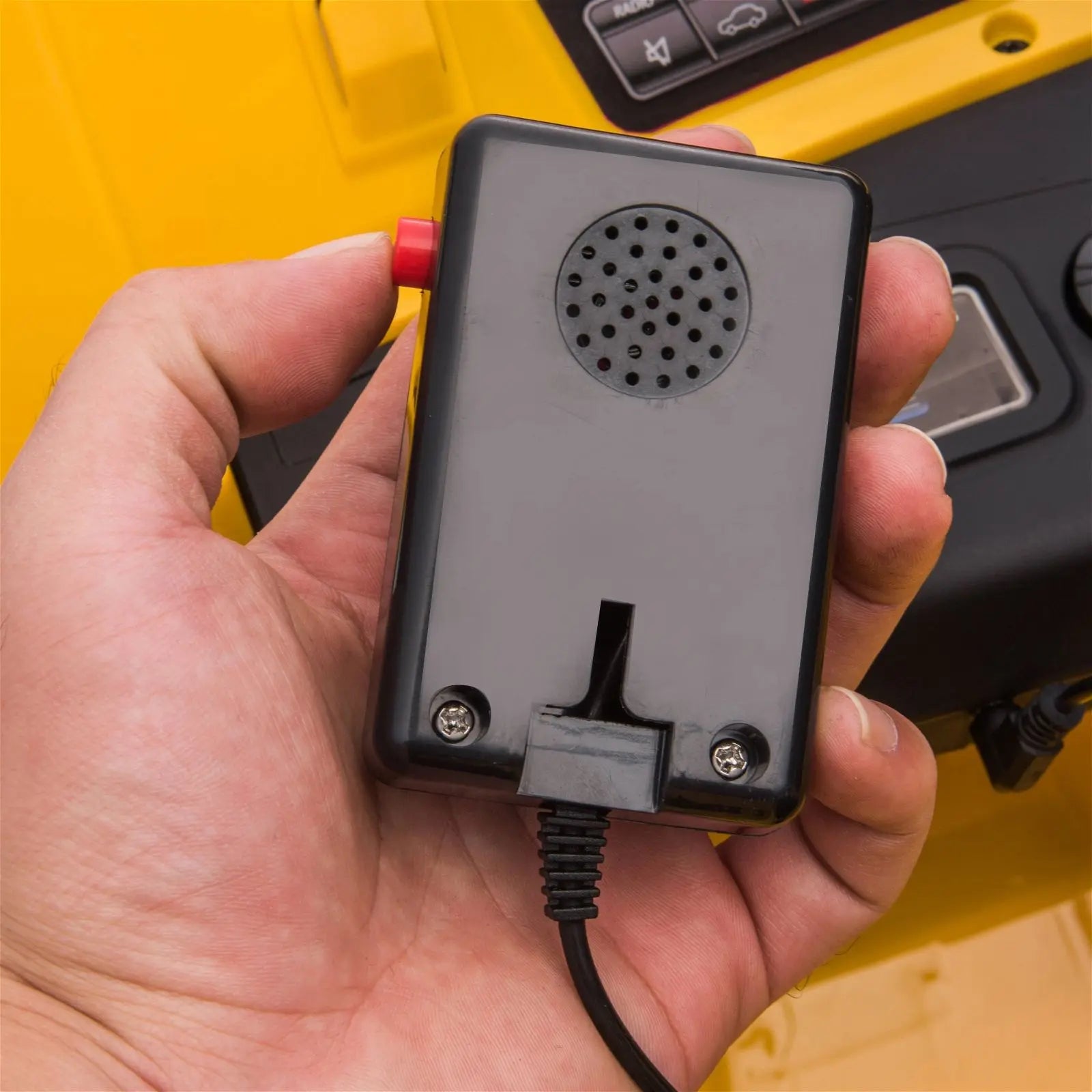 Close-up of a person holding a wired black remote control in a yellow toy vehicle cockpit.
