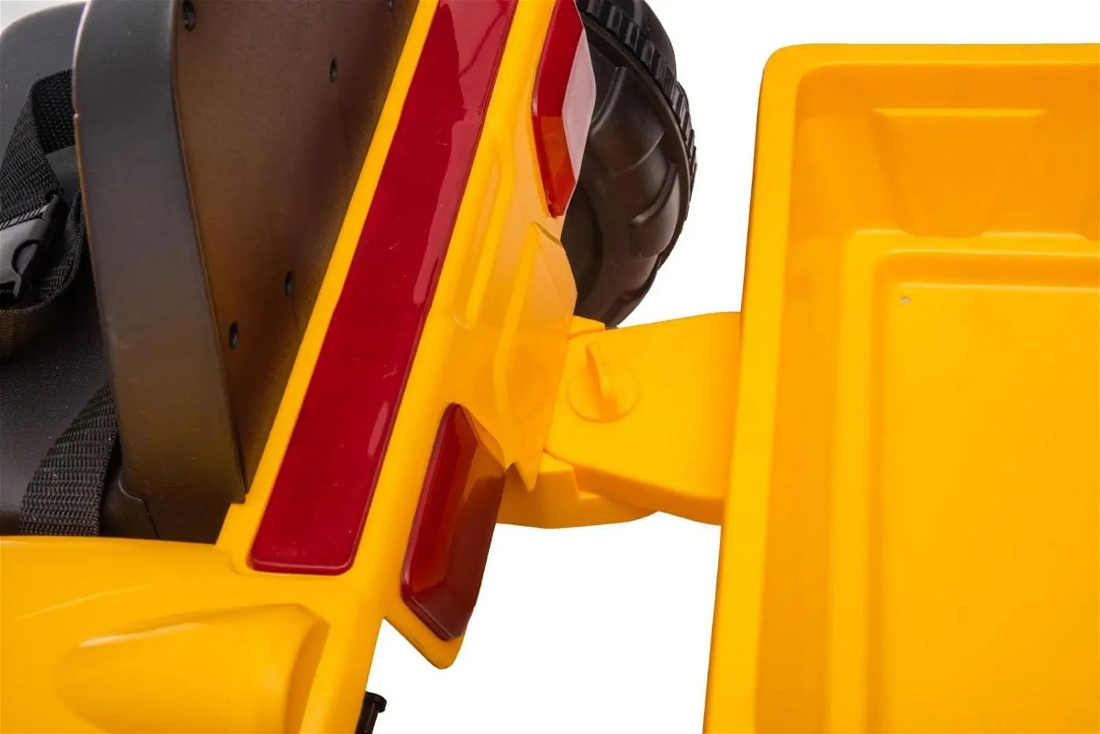 Close-up of yellow ride-on toy excavator seat and dump bed, black wheel visible