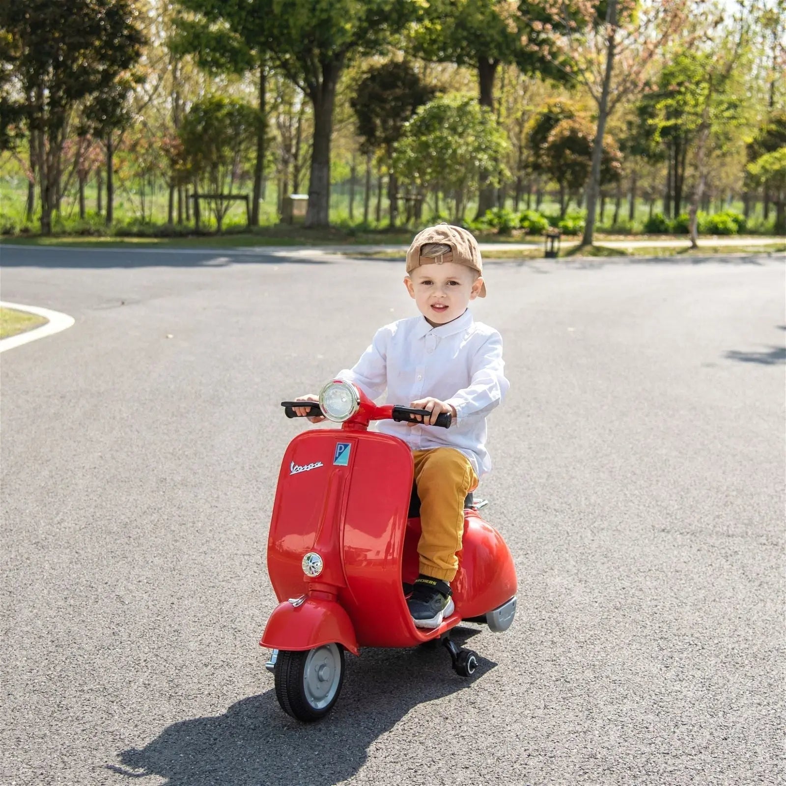 Child riding red 12V kids electric Vespa scooter outdoors on paved path