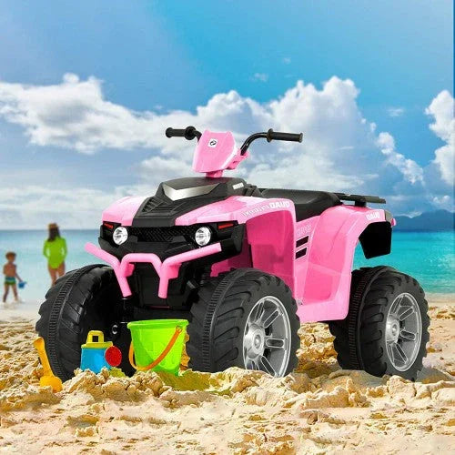 Pink 12V kids ride-on ATV on sandy beach with colorful sand toys and ocean background