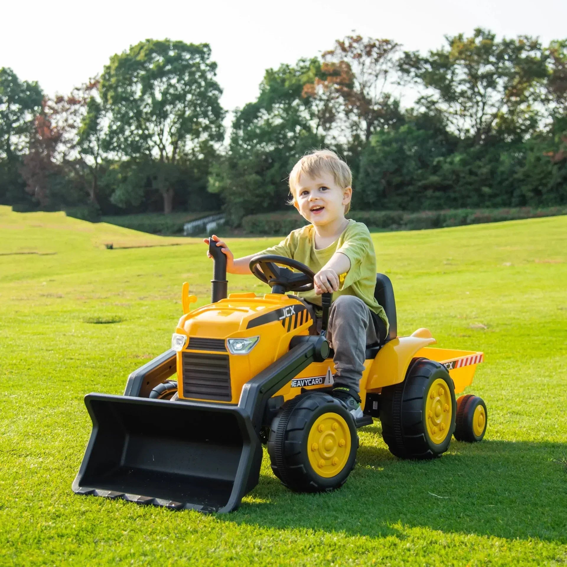 Child riding yellow 12V Freddo excavator ride-on toy tractor on grassy field