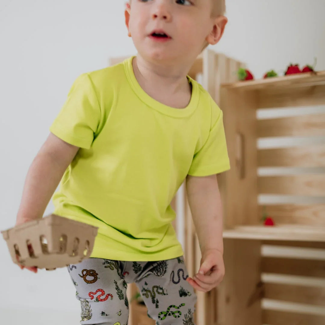 Toddler in yellow shirt holding berry basket, wooden crates and strawberries behind
