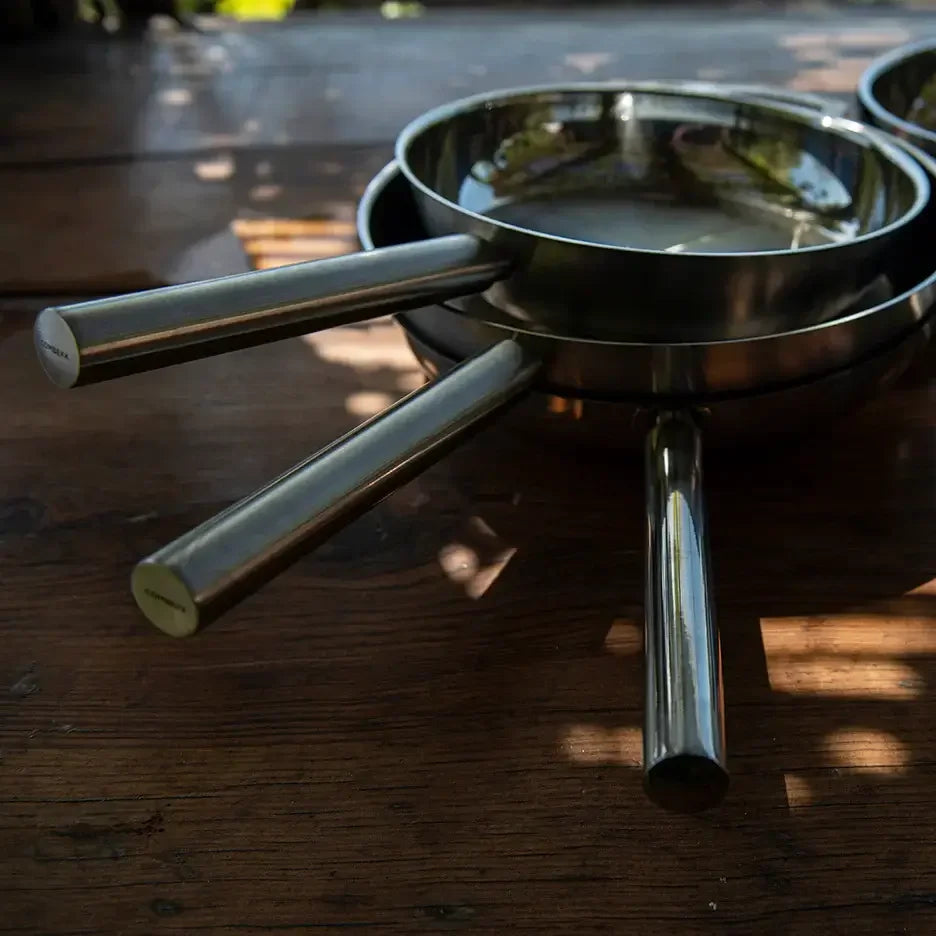 Stack of stainless steel camping frying pans with metal handles on wooden table outdoors
