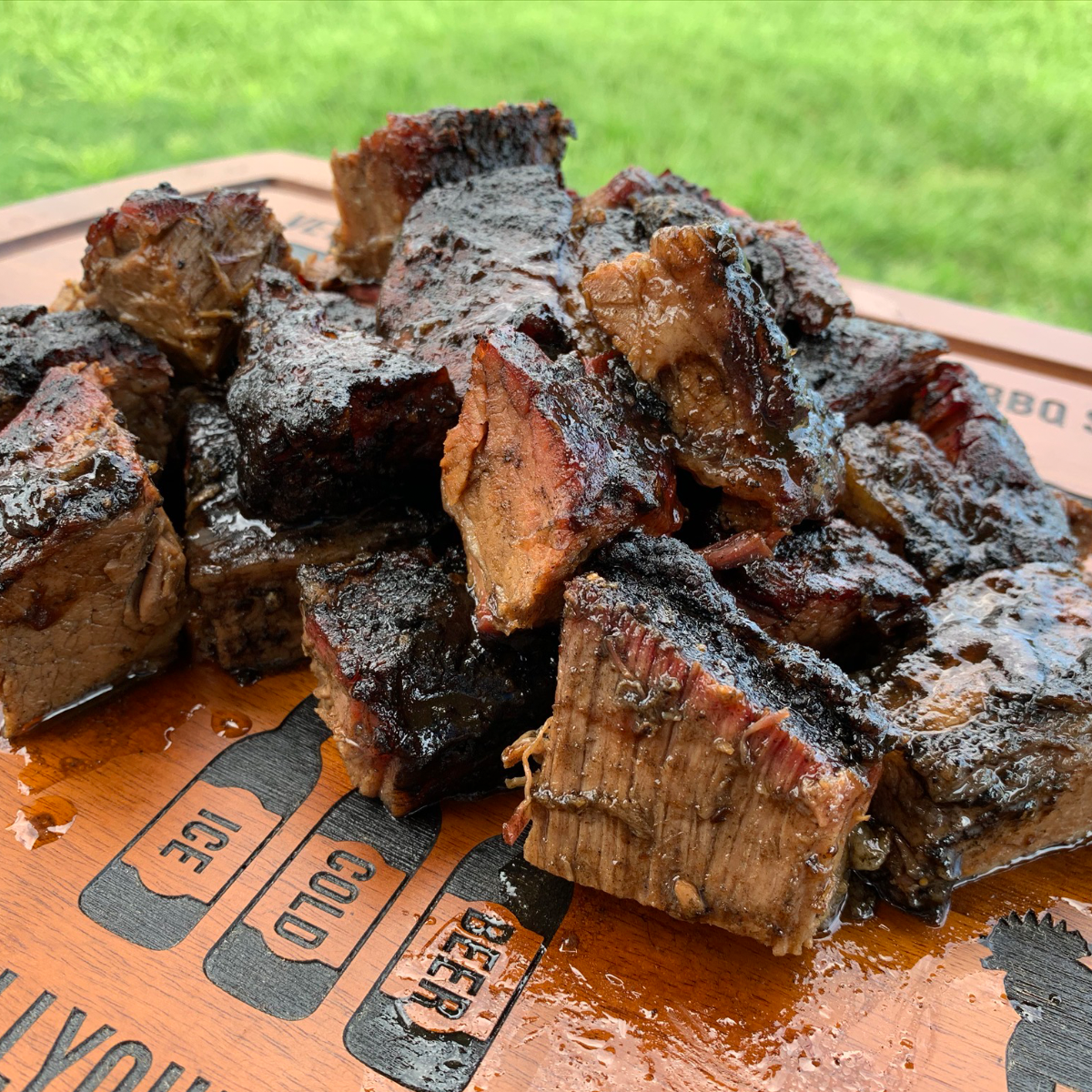 Juicy smoked brisket burnt ends on a wooden cutting board outdoors, perfect for camping BBQ.