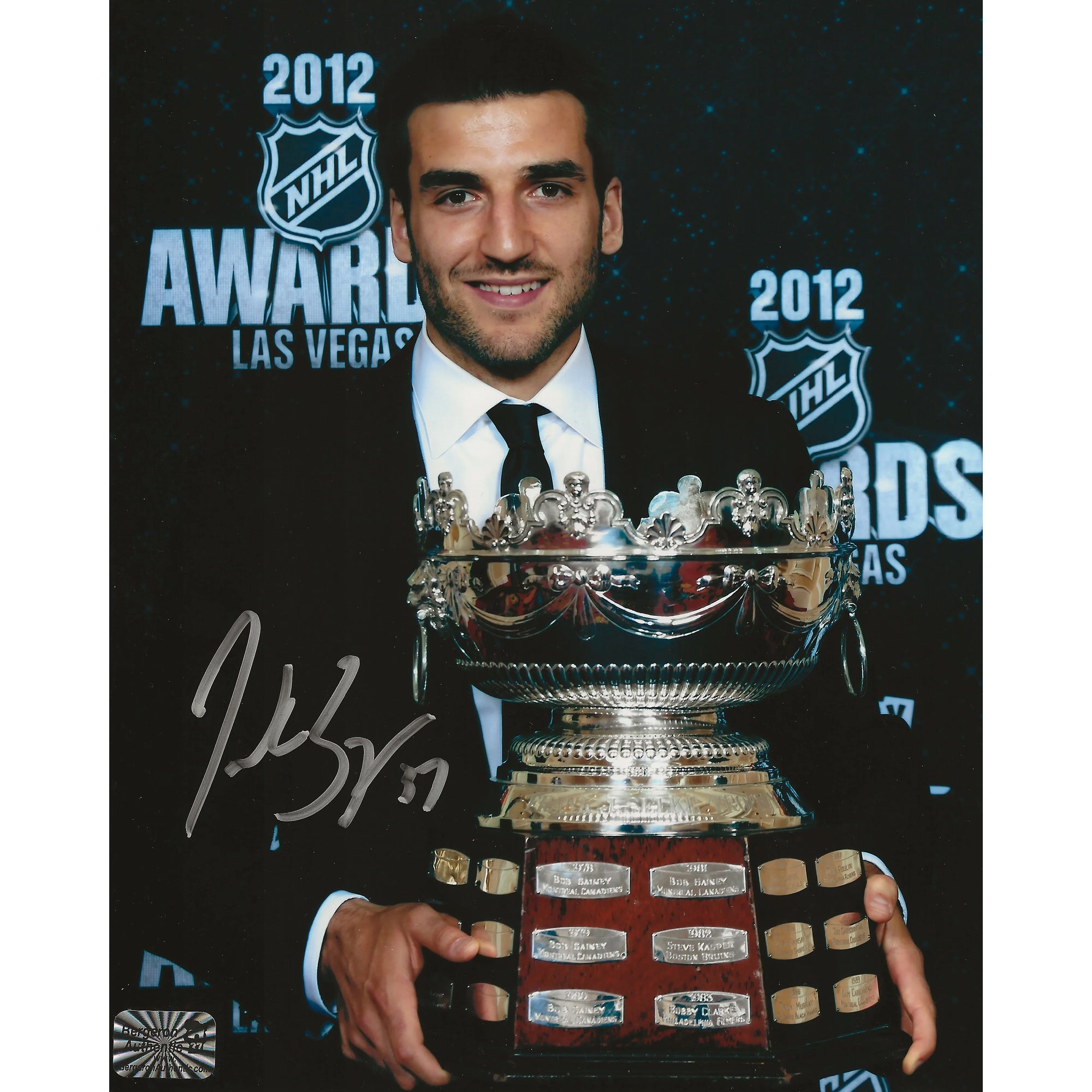 Smiling man in suit holding large silver hockey trophy at 2012 NHL Awards in Las Vegas