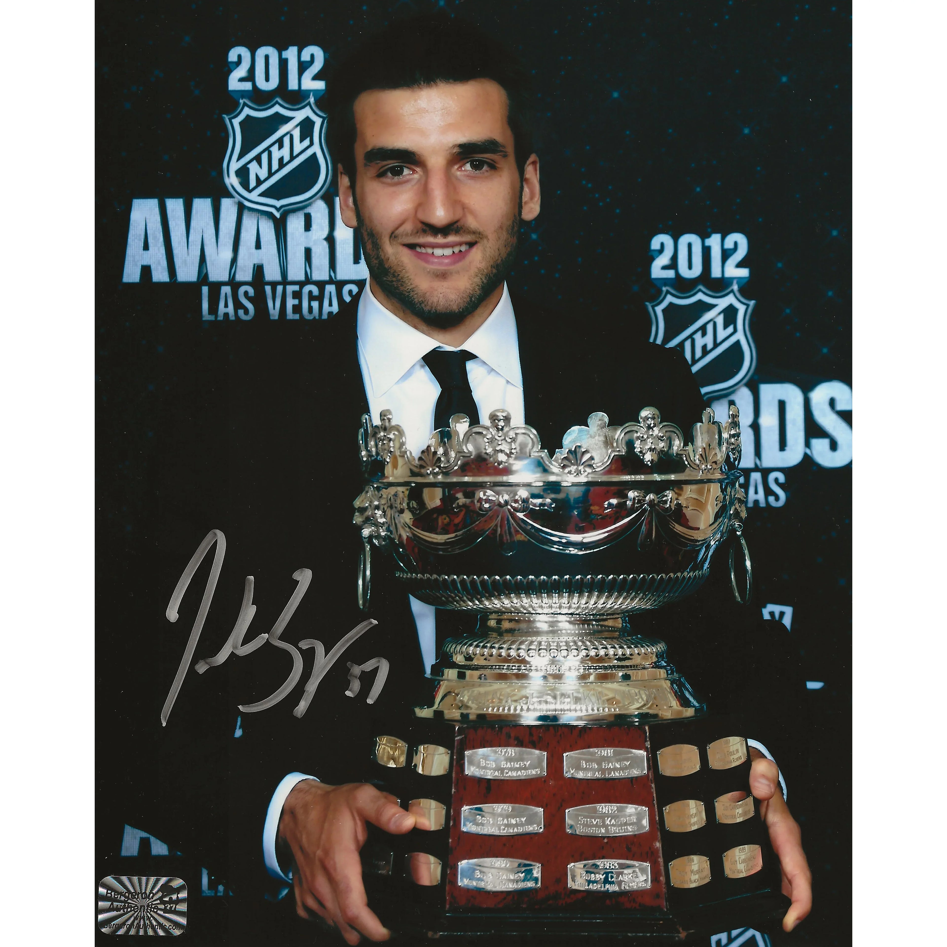 Smiling man in suit holding large silver hockey trophy at 2012 NHL Awards in Las Vegas