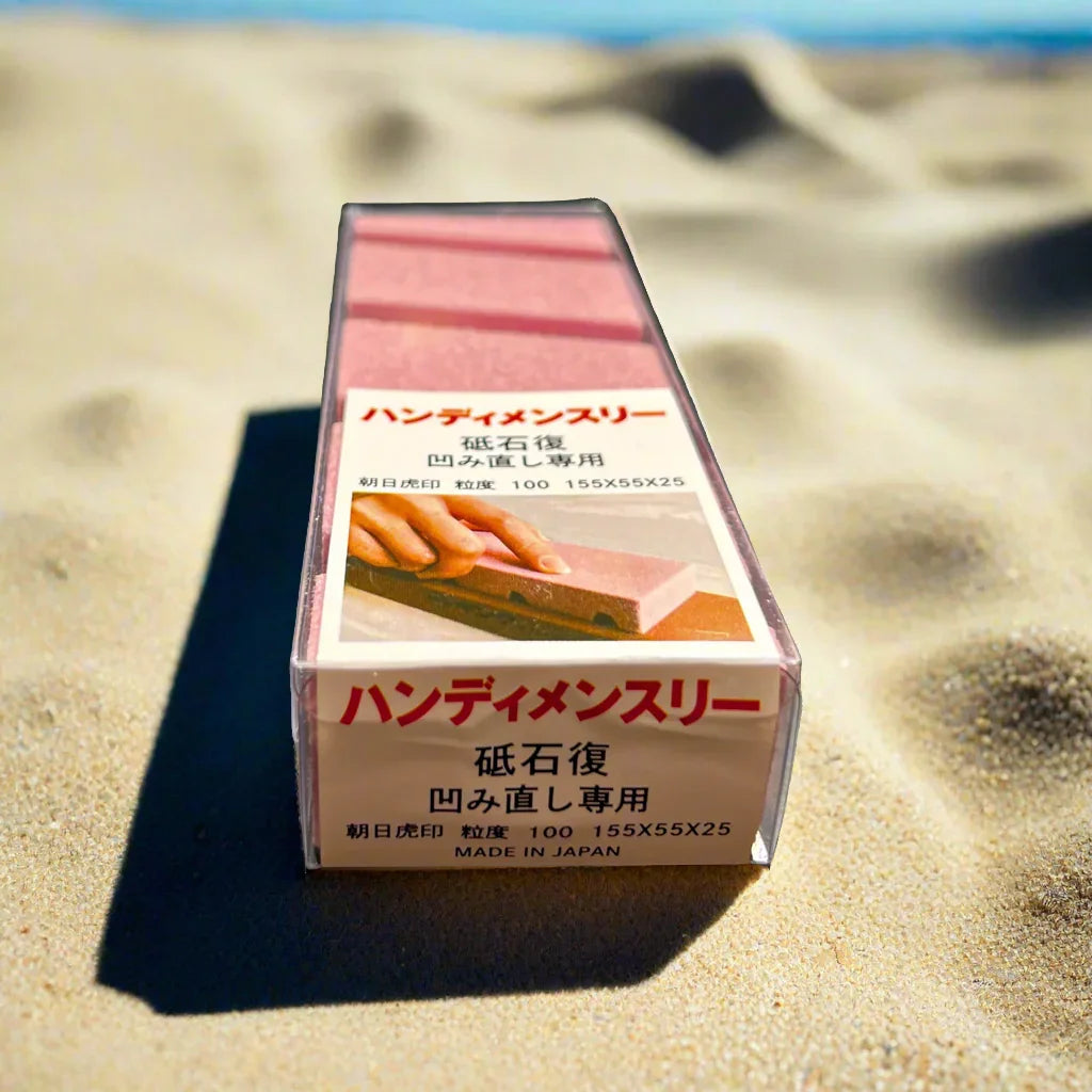Pink Japanese sharpening stone in box on sand, outdoor camping gear focus