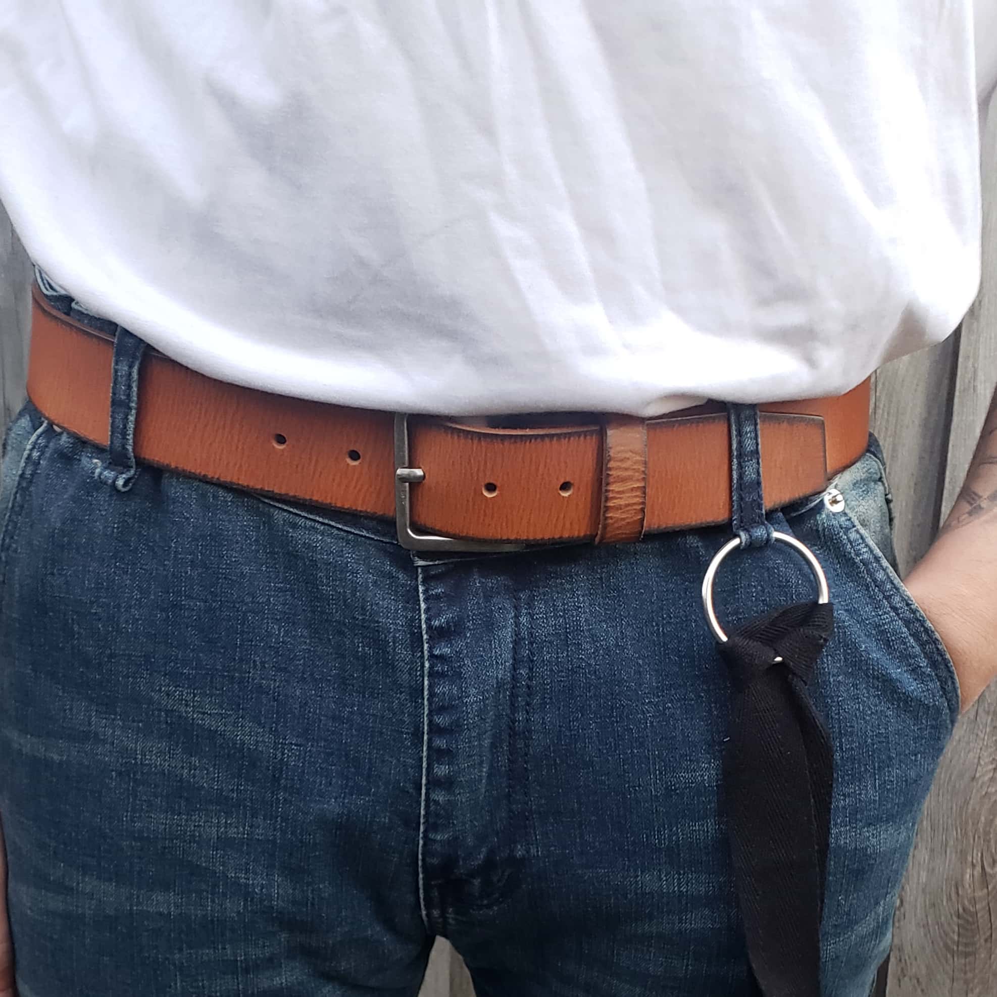 Brown leather belt with metal buckle worn on blue jeans and white shirt outdoors