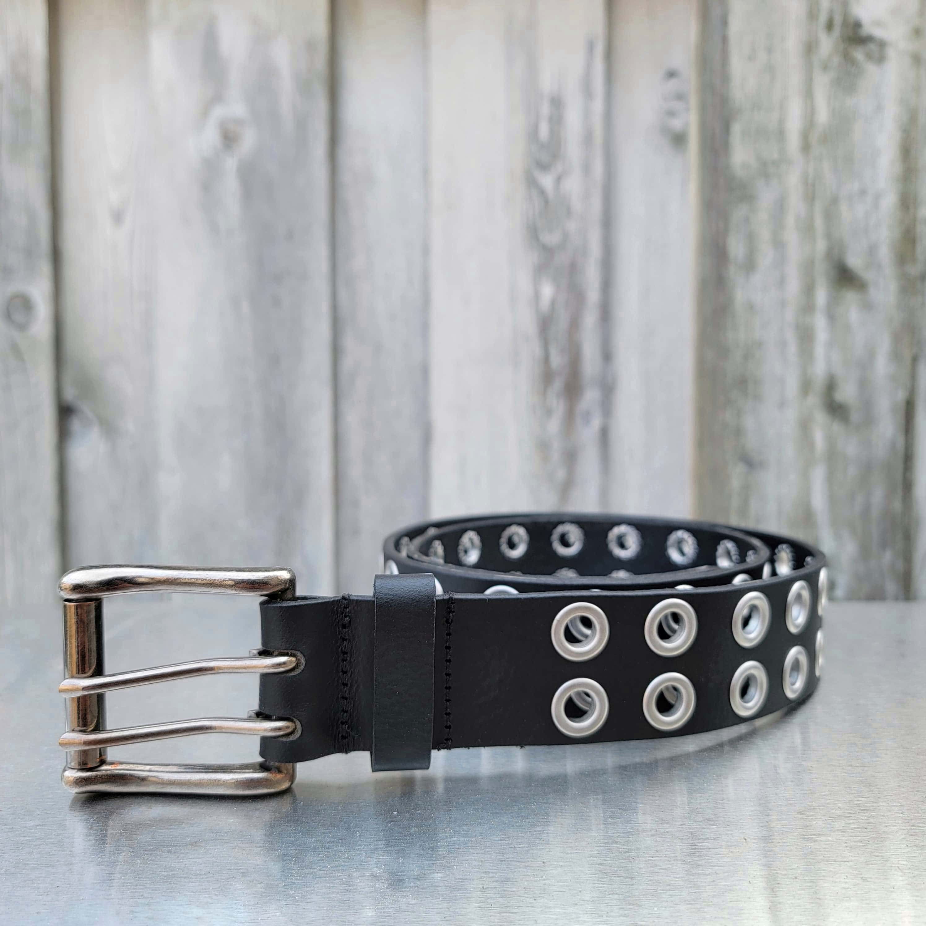 Black leather double grommet belt with silver buckle on outdoor metal surface