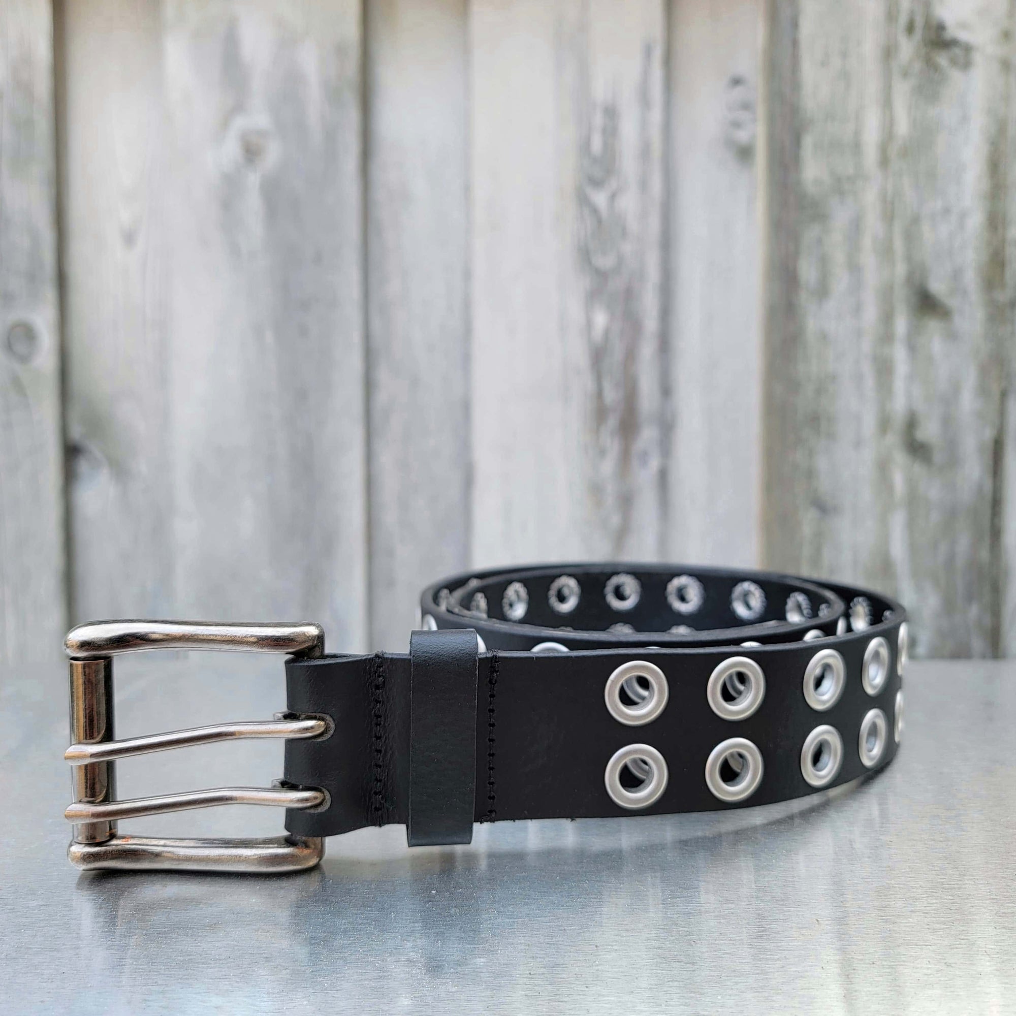 Black leather double grommet belt with silver buckle on outdoor metal surface