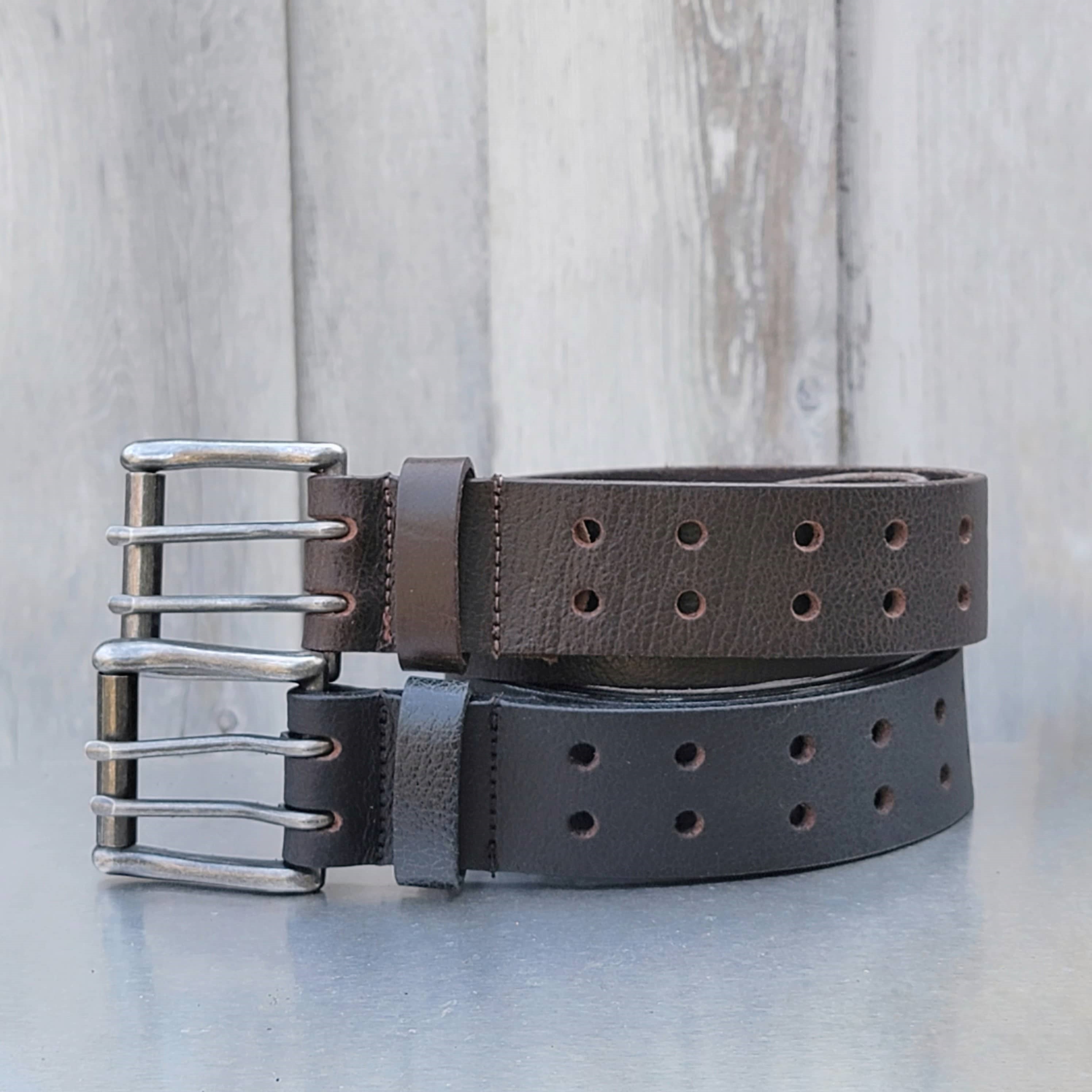 Two heavy-duty leather belts with double prong buckles, brown and black, on rustic background