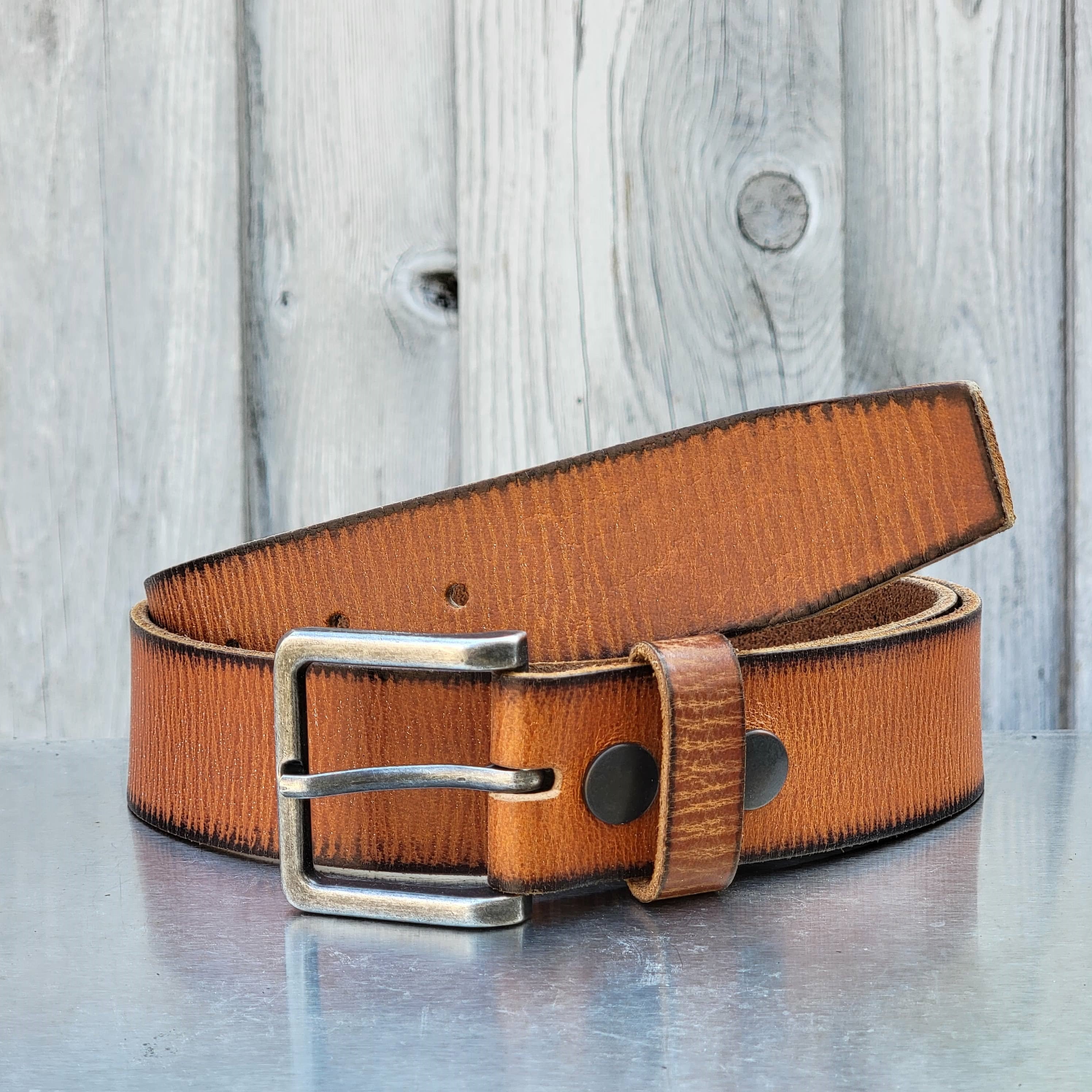 Brown leather belt with metal buckle for outdoor apparel, displayed on rustic wood background