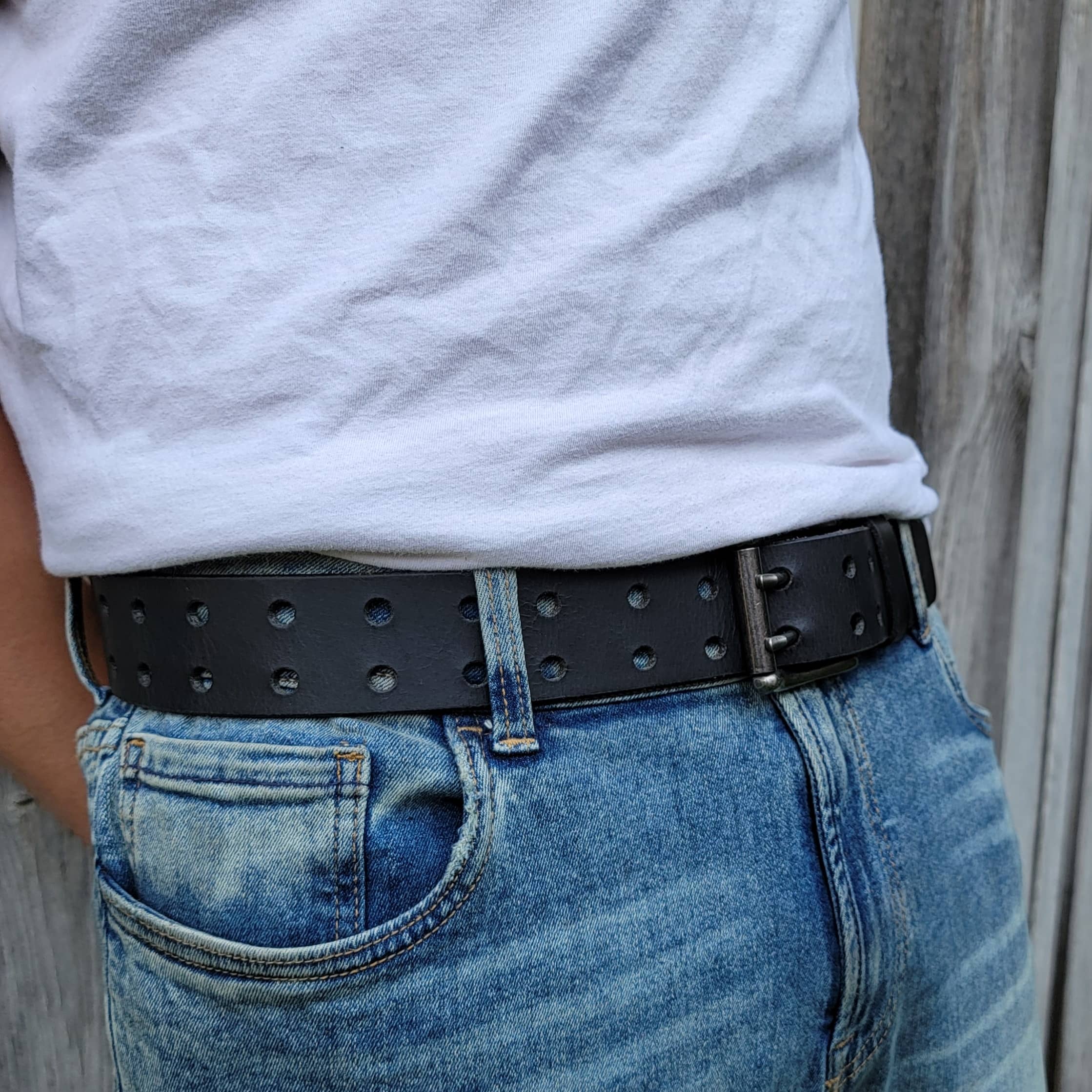Black tactical belt with double buckle and holes, worn with blue jeans outdoors