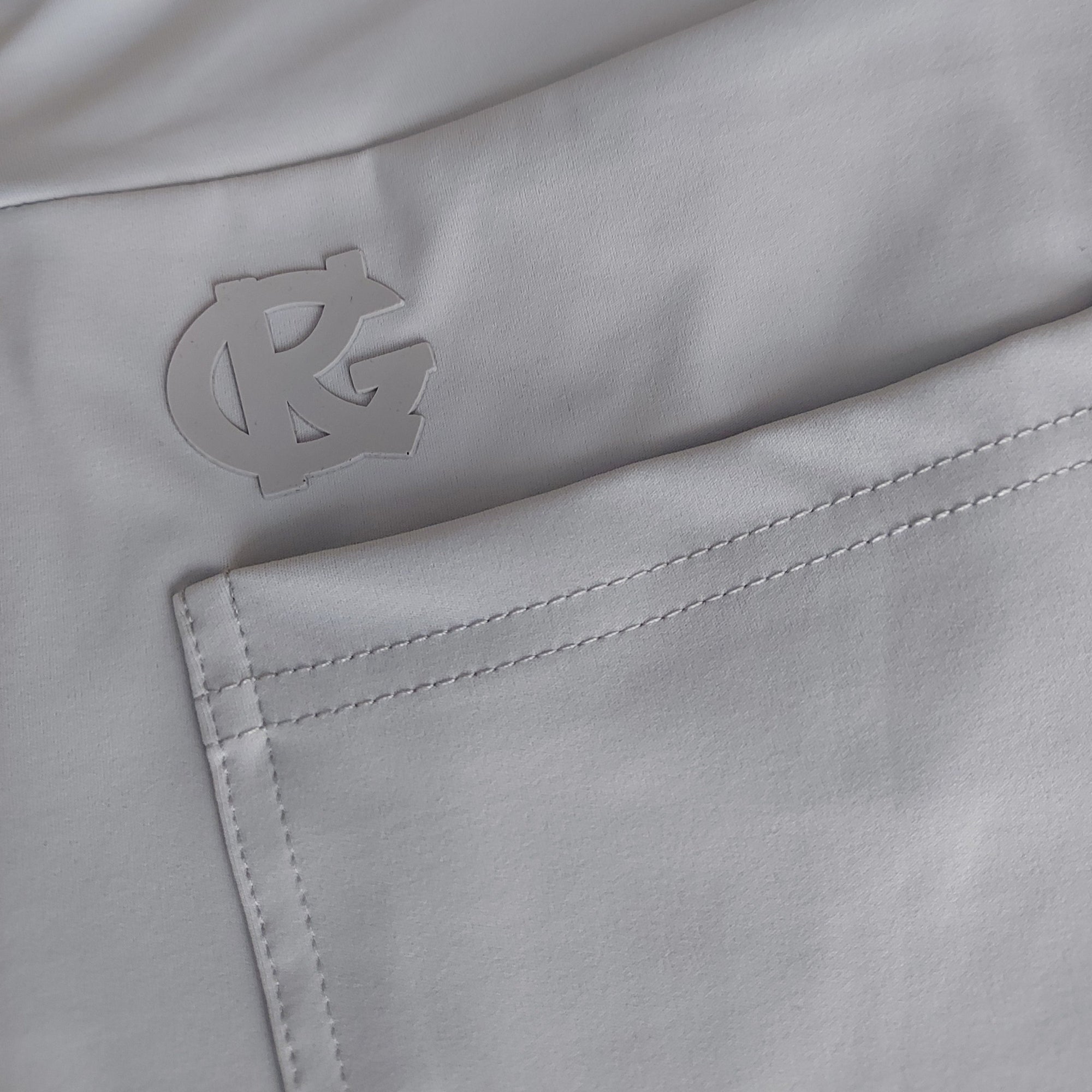 Close-up of light grey technical outdoor apparel with stitched pocket and raised logo detail.