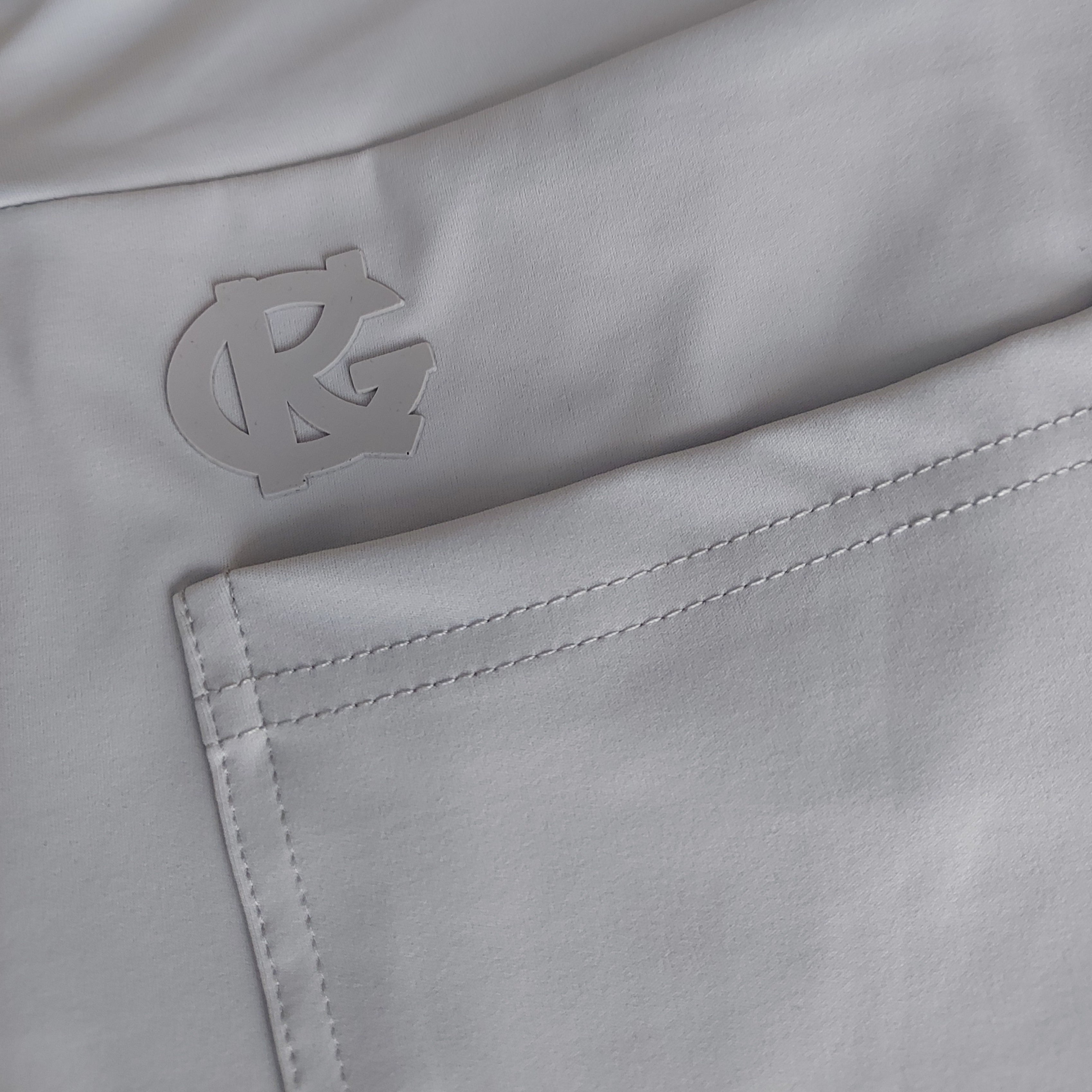 Close-up of light grey technical outdoor apparel with stitched pocket and raised logo detail.