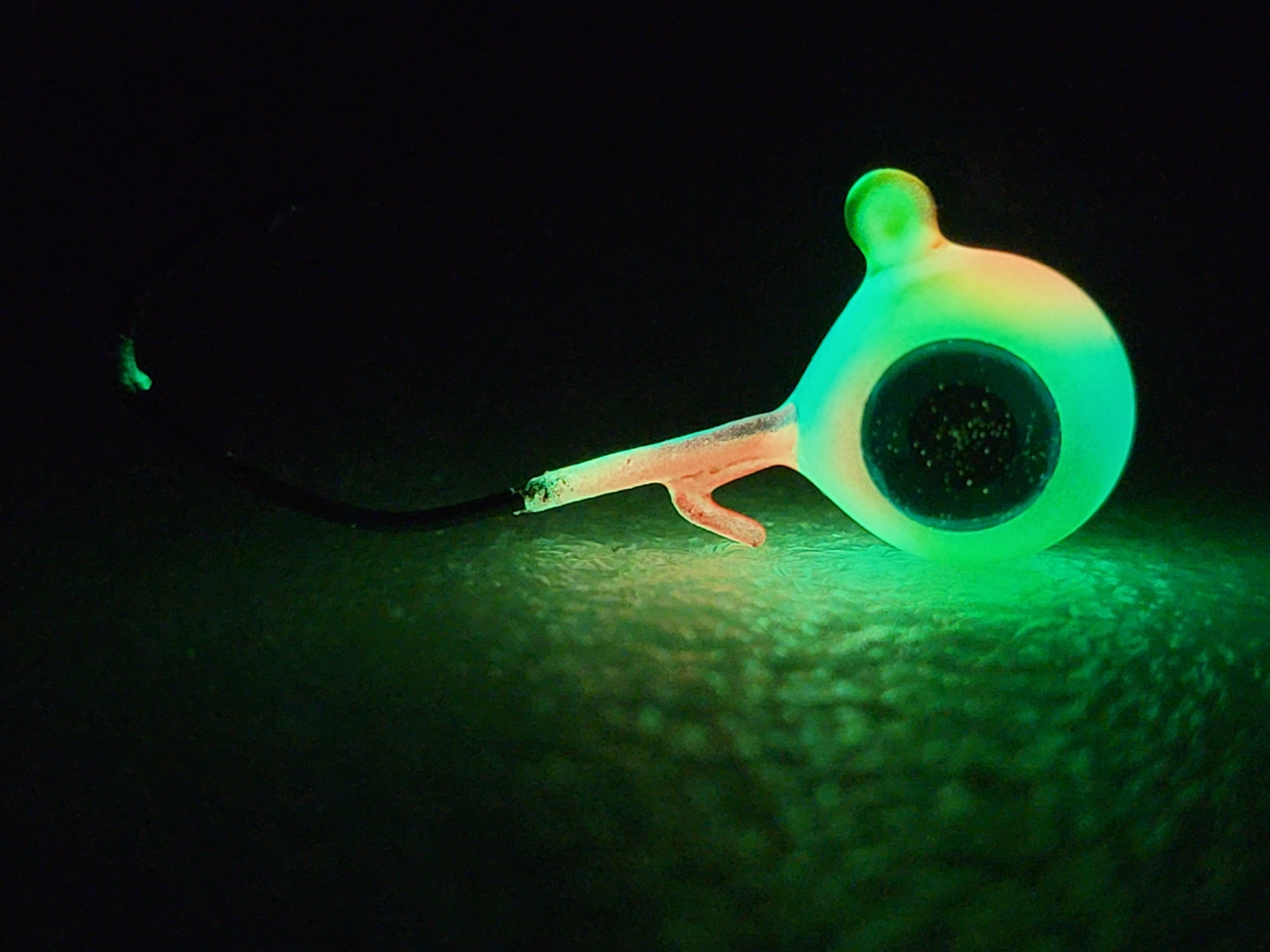 Glowing green fishing lure for night fishing on dark textured surface