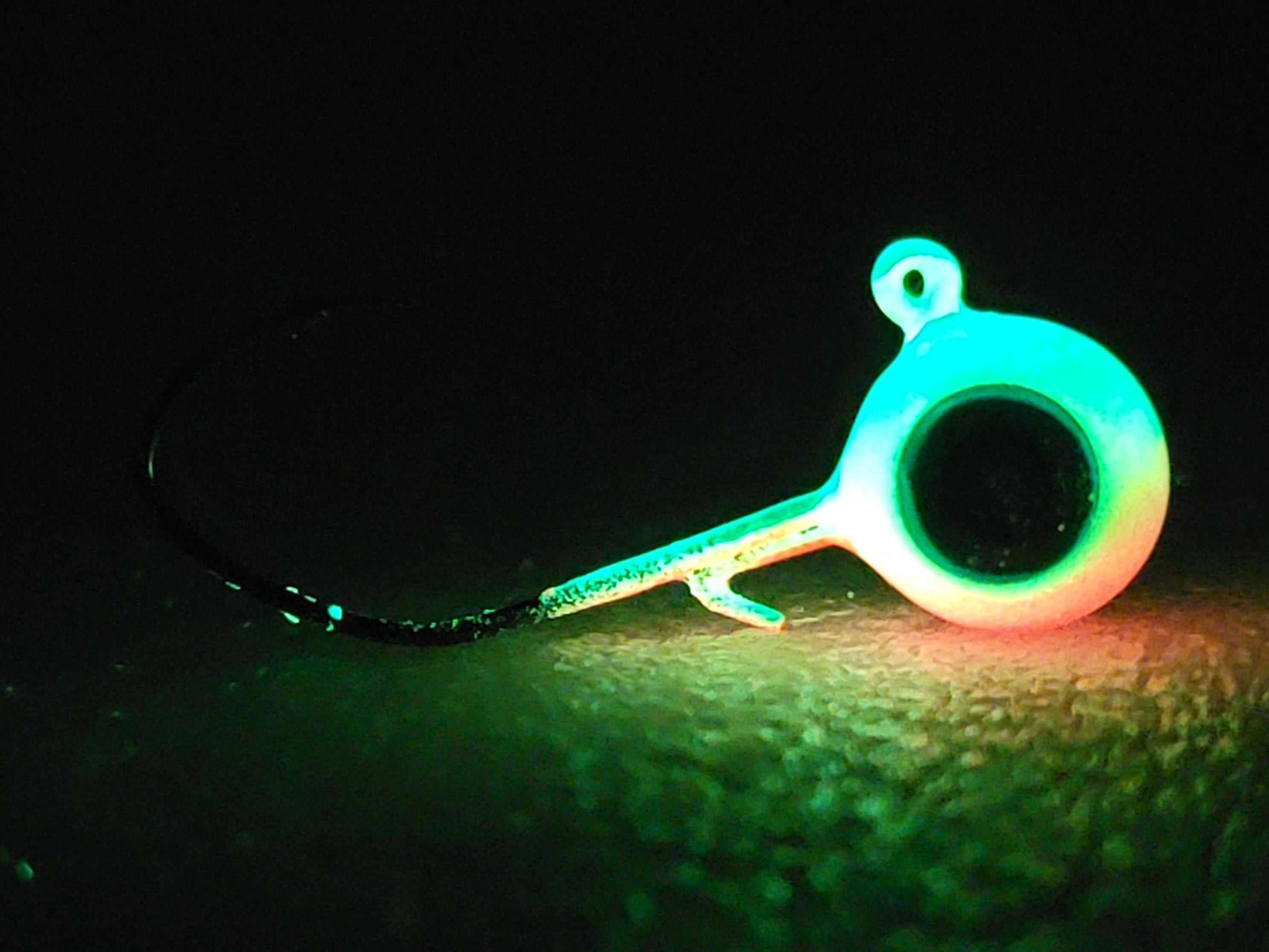 Glow in the dark fishing jig head with hook, vivid green and orange, on dark surface