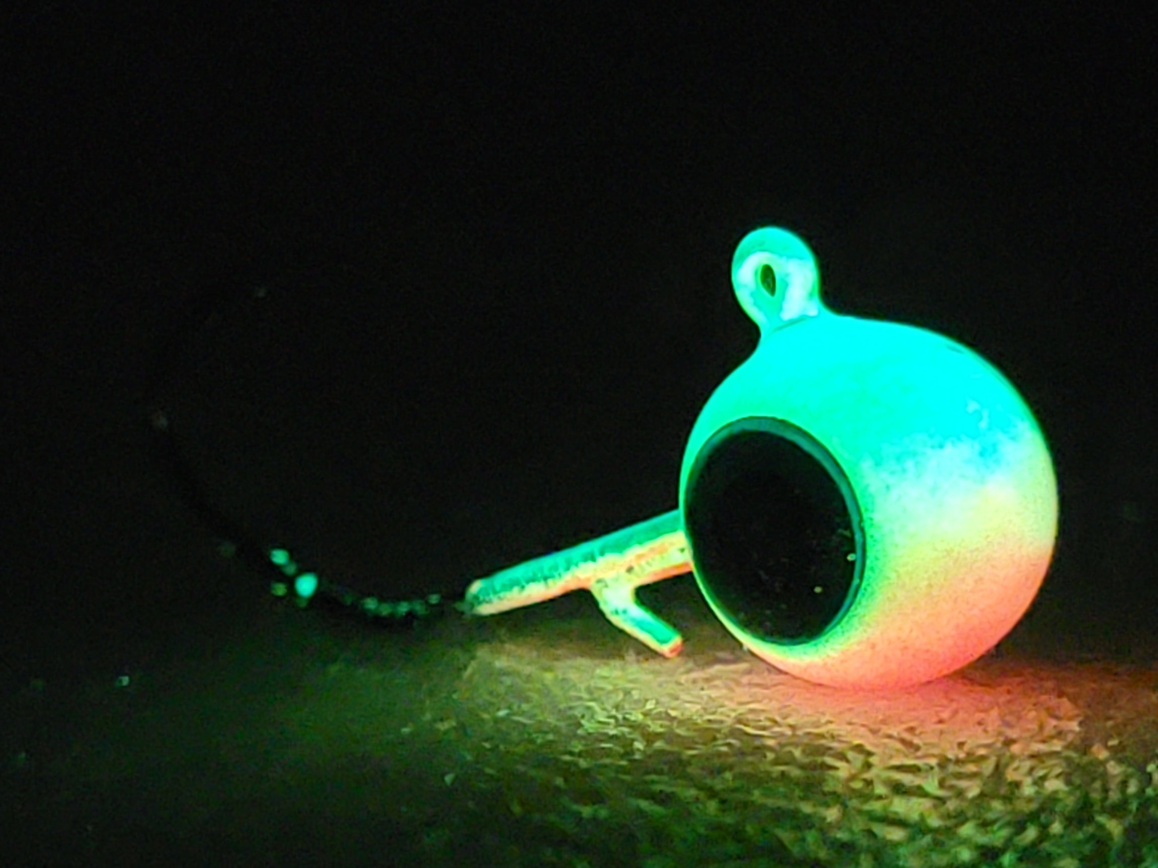Glow in the dark fishing jig head with black eye detail on textured surface, night visibility lure