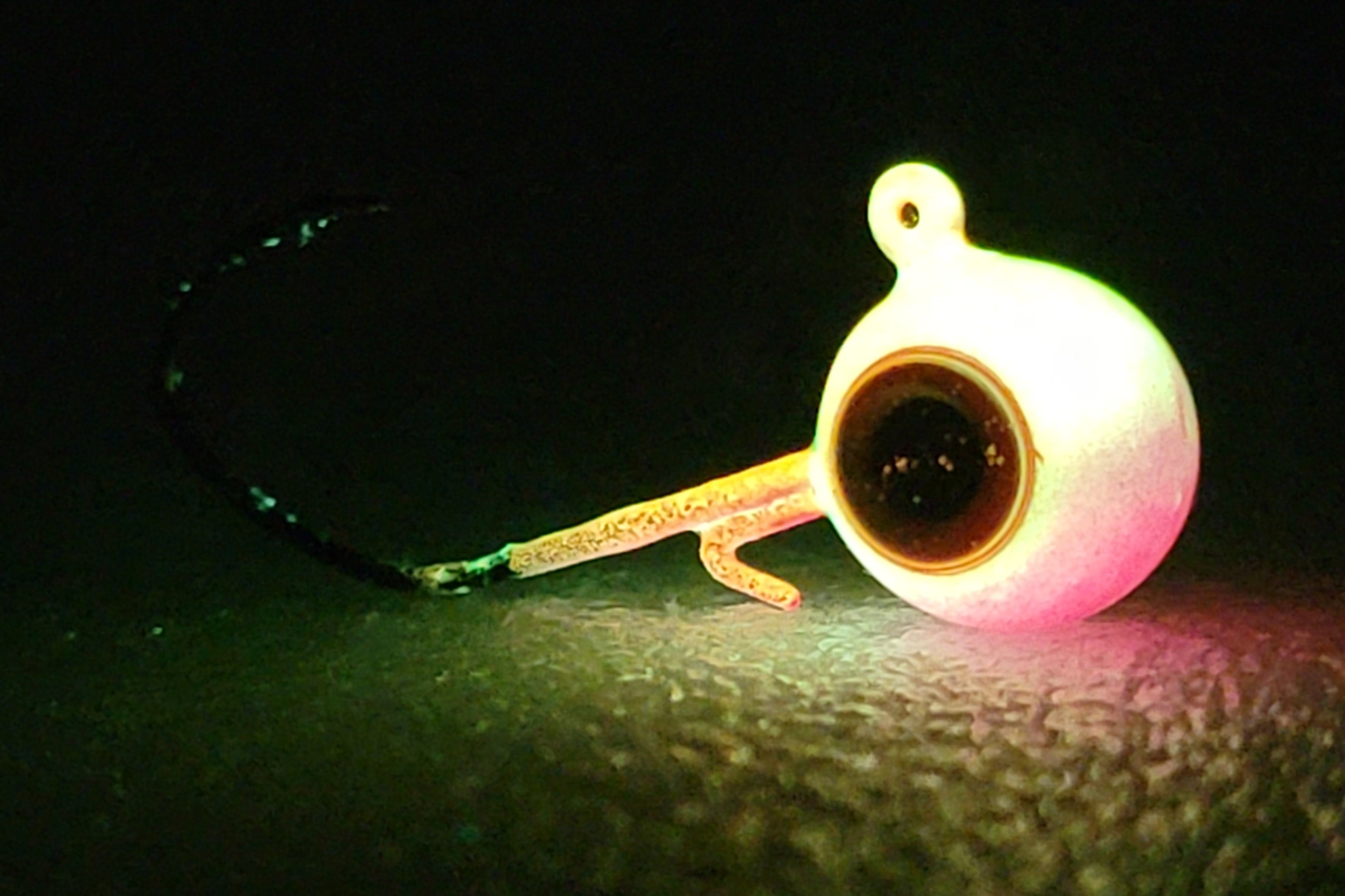 Glowing fishing jig head with hook on dark textured surface, night fishing gear