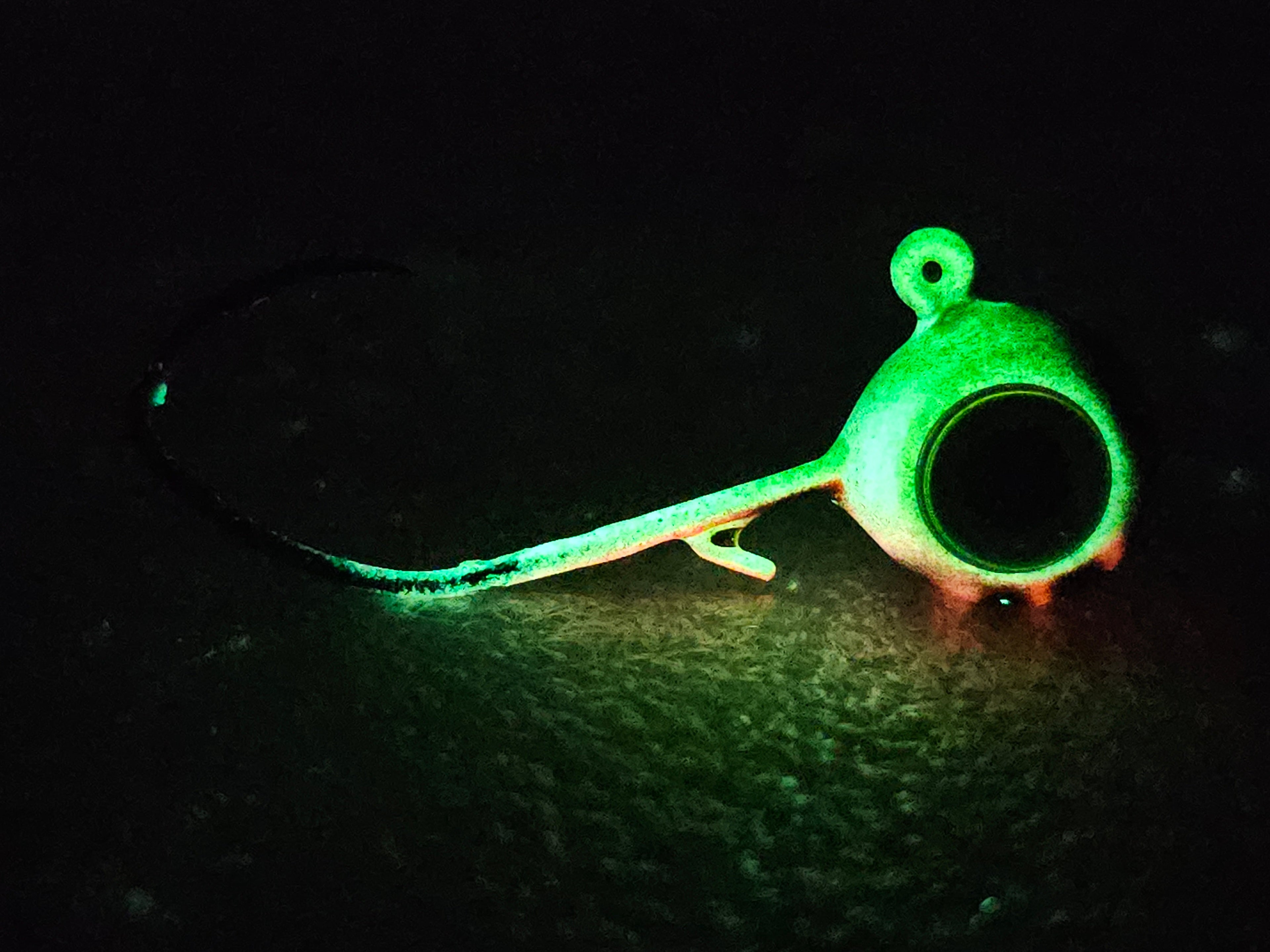 Glow-in-the-dark fishing jig head on textured dark surface, ideal for night fishing