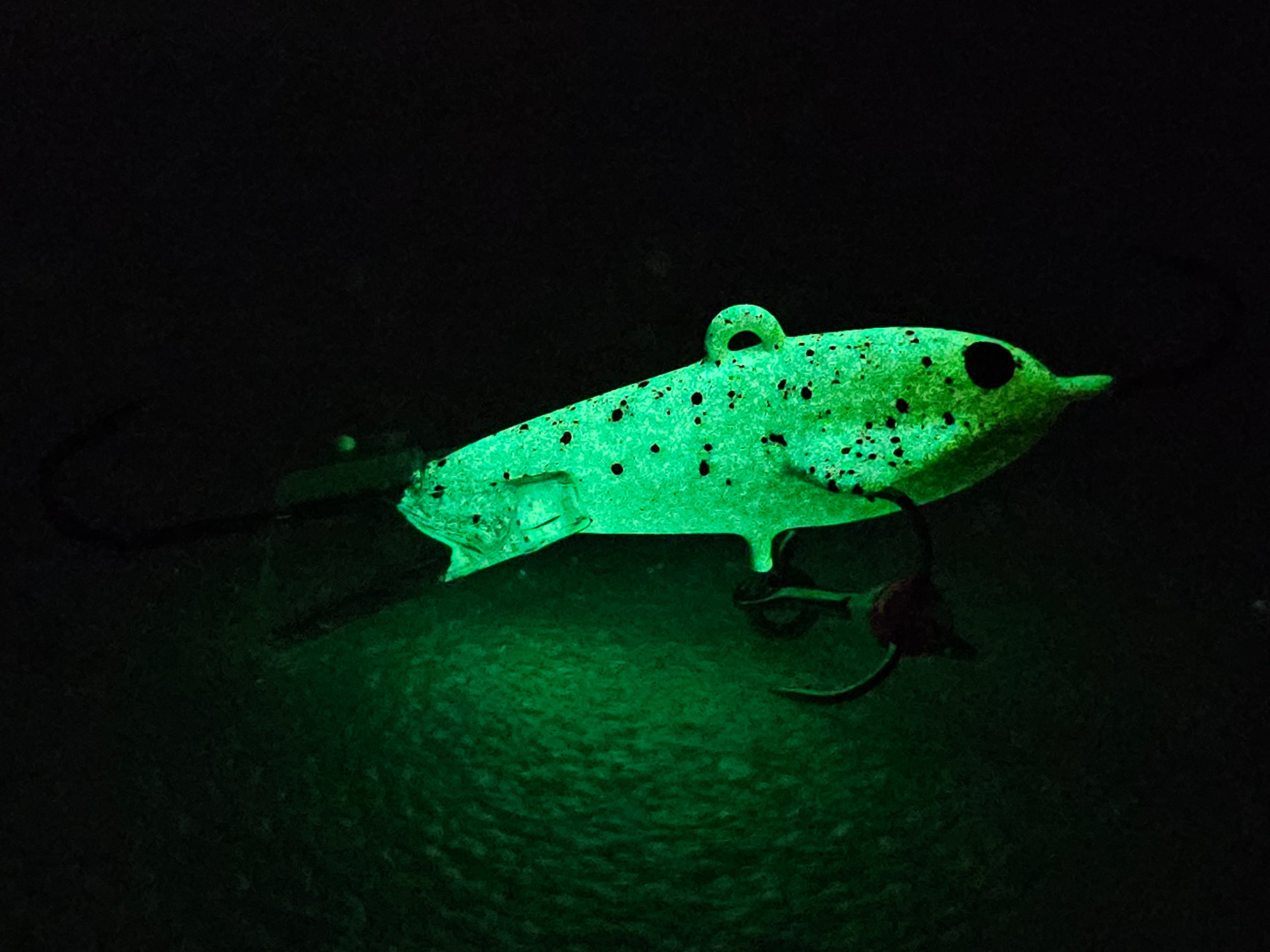 Glowing green fishing lure with black spots and hooks in dark setting