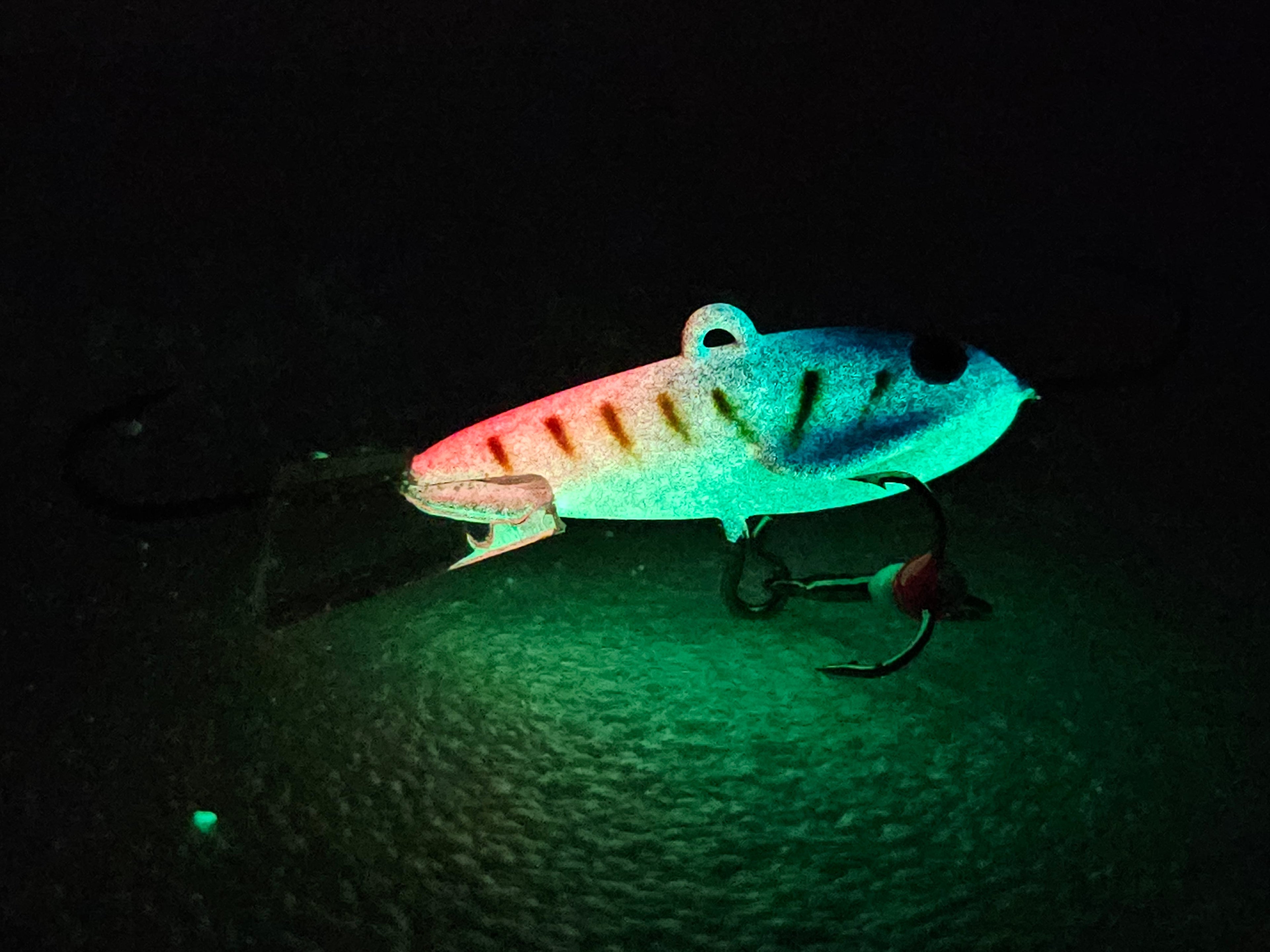 Glow-in-the-dark fishing lure with treble hook on textured surface at night