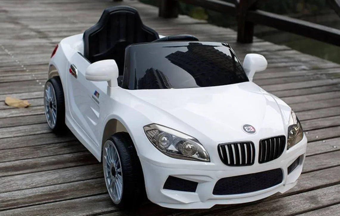 White kids electric ride-on toy car with black seat on wooden deck outdoors