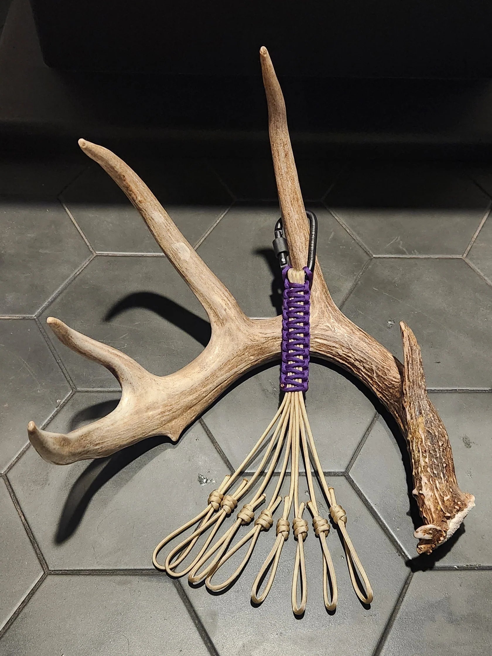 Deer antler game call lanyard with paracord loops on a hexagon tile floor, hunting gear.