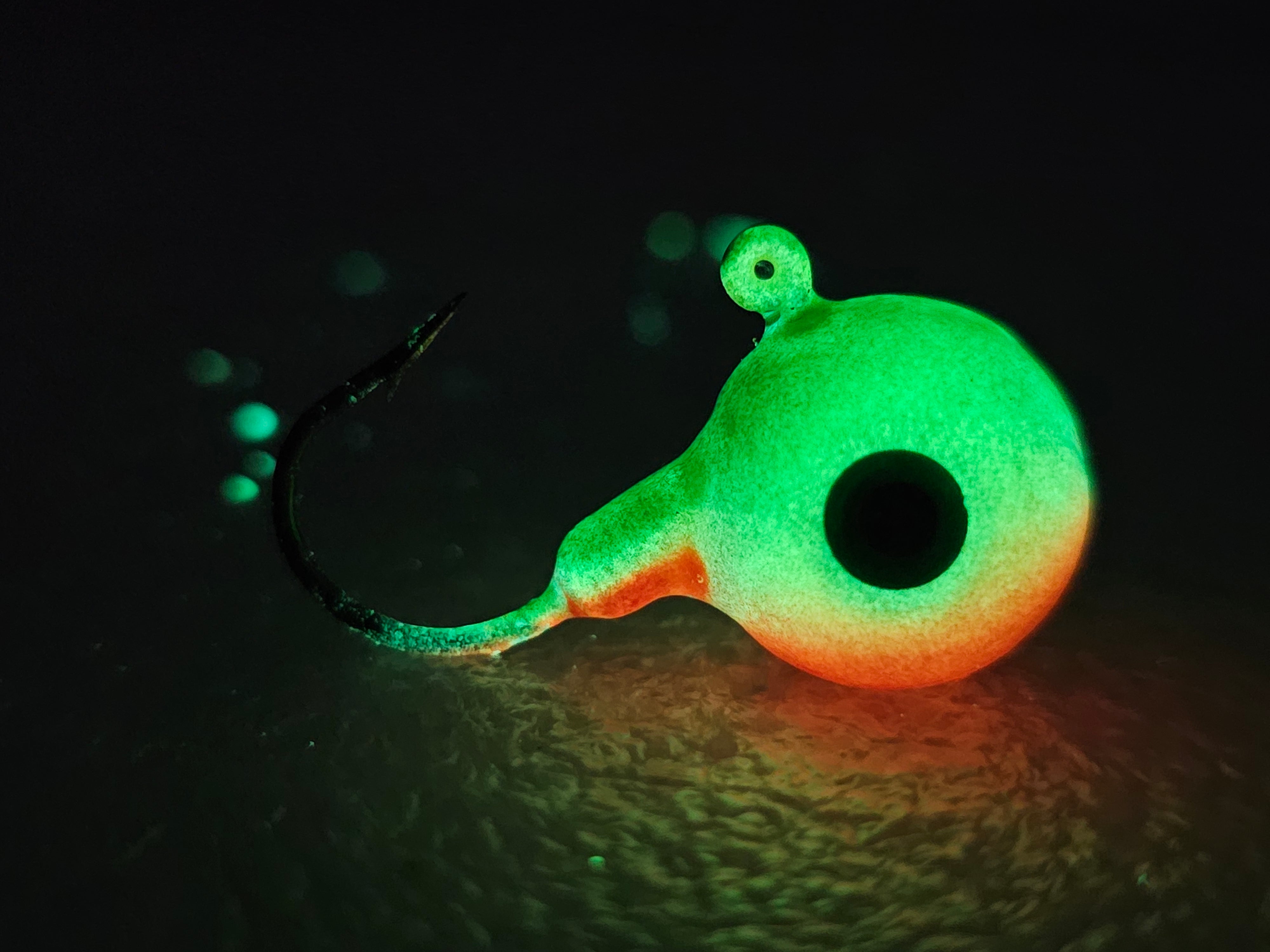Glow-in-the-dark fishing jig lure with green and orange colors on dark background