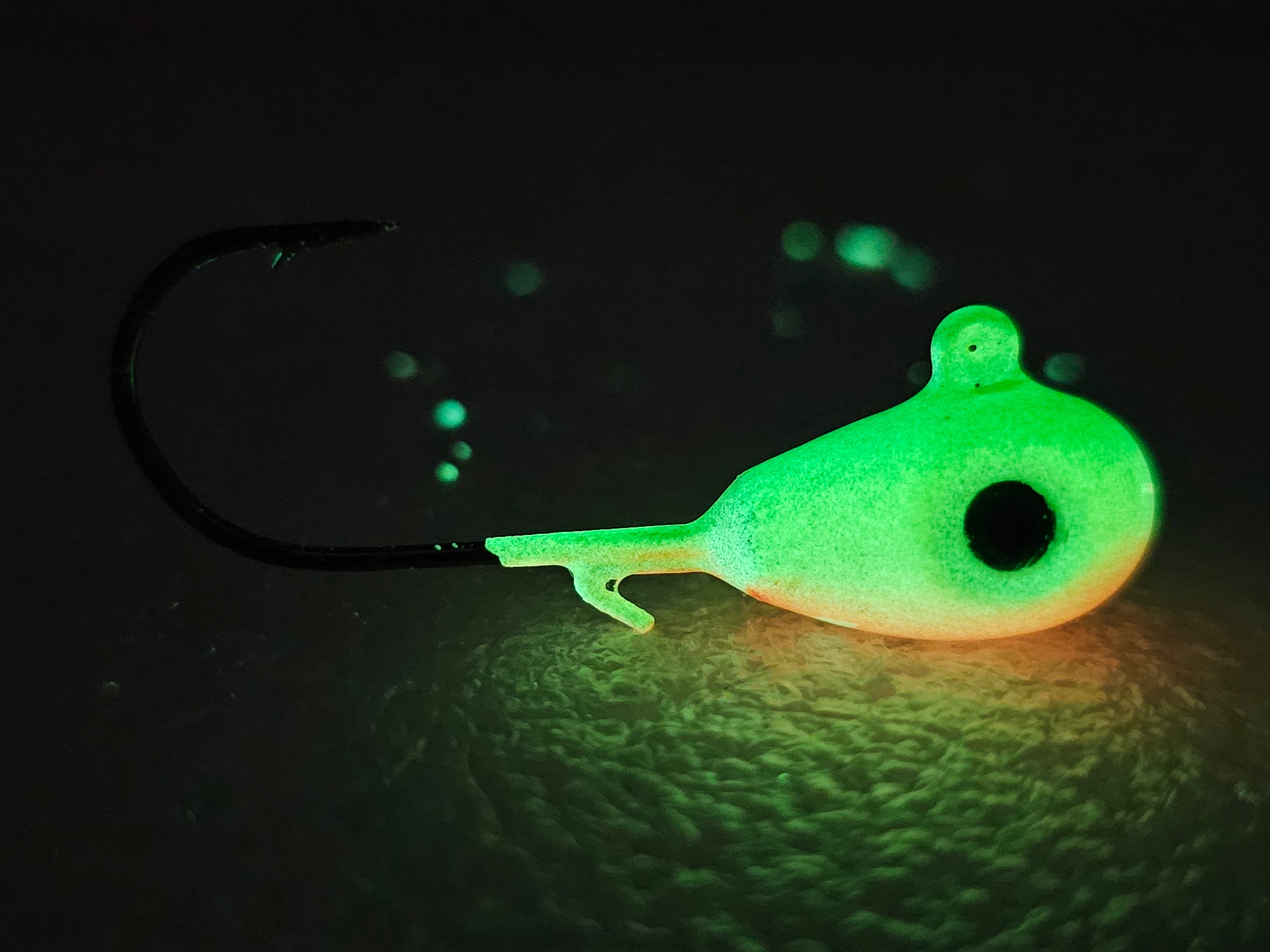 Glow-in-the-dark fishing jig head with hook on dark textured surface