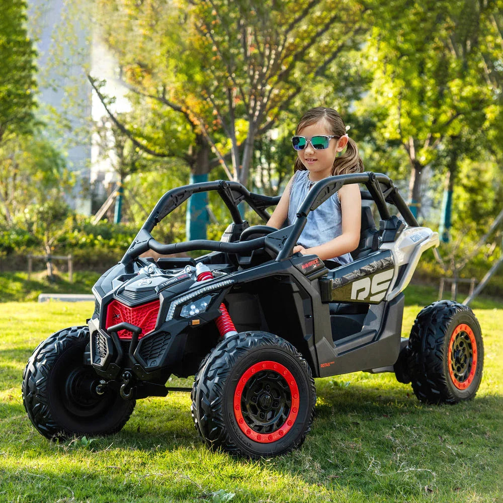 Girl wearing sunglasses driving a black and red electric ride-on toy car outdoors on grass