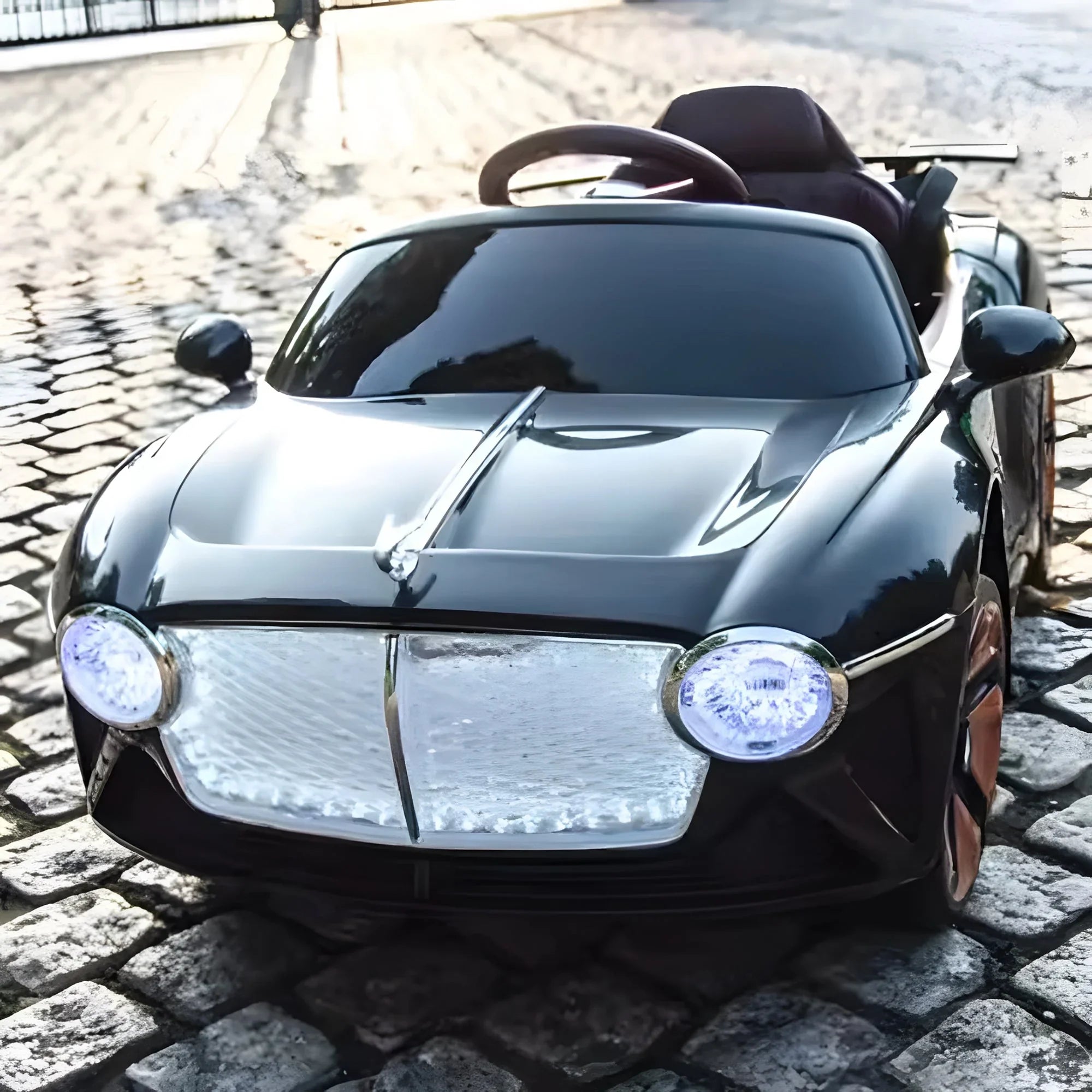 Black kids' ride on car toy with LED headlights on cobblestone street