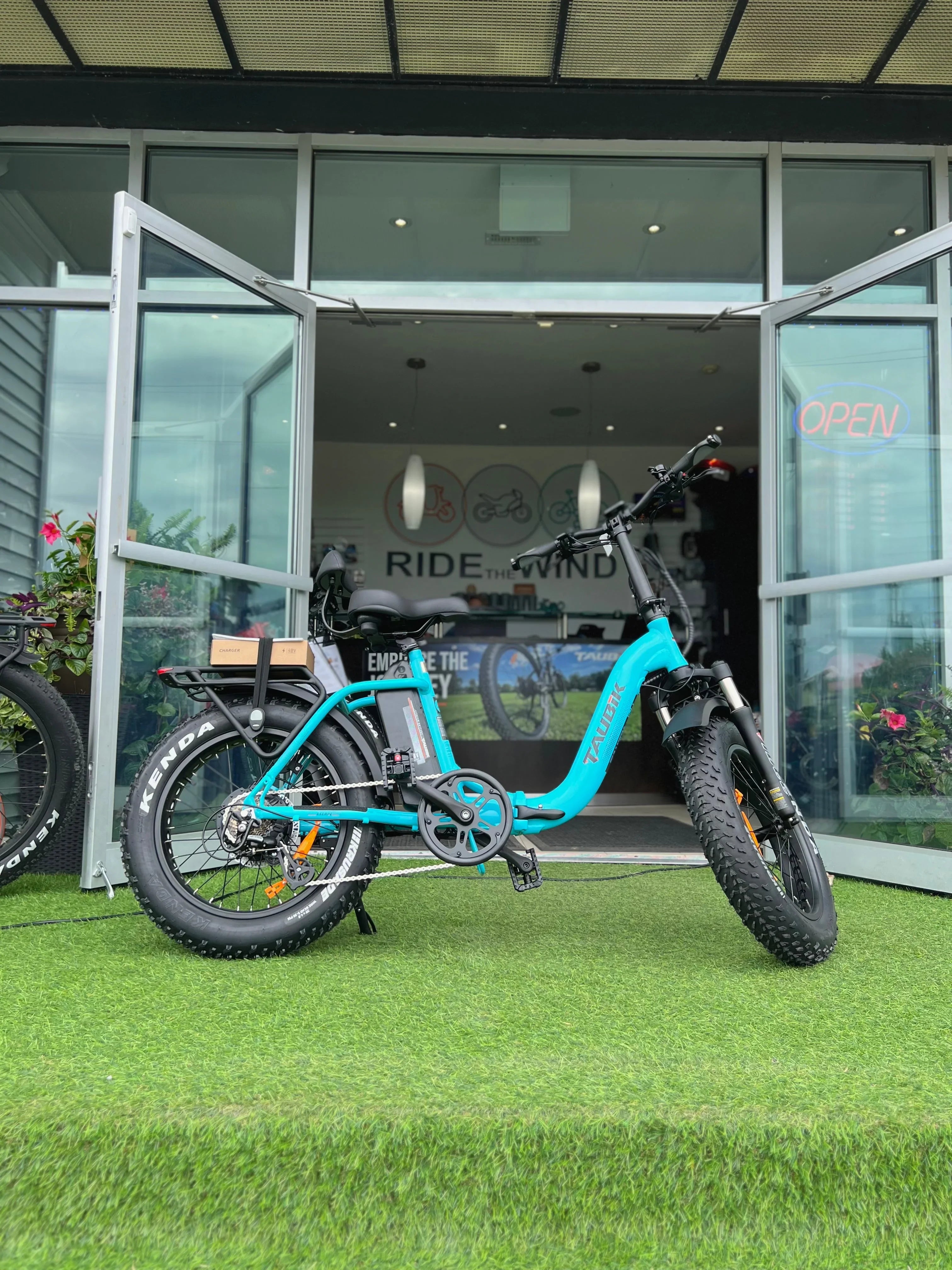 Blue fat tire electric bike parked on artificial grass outside a shop with open doors.