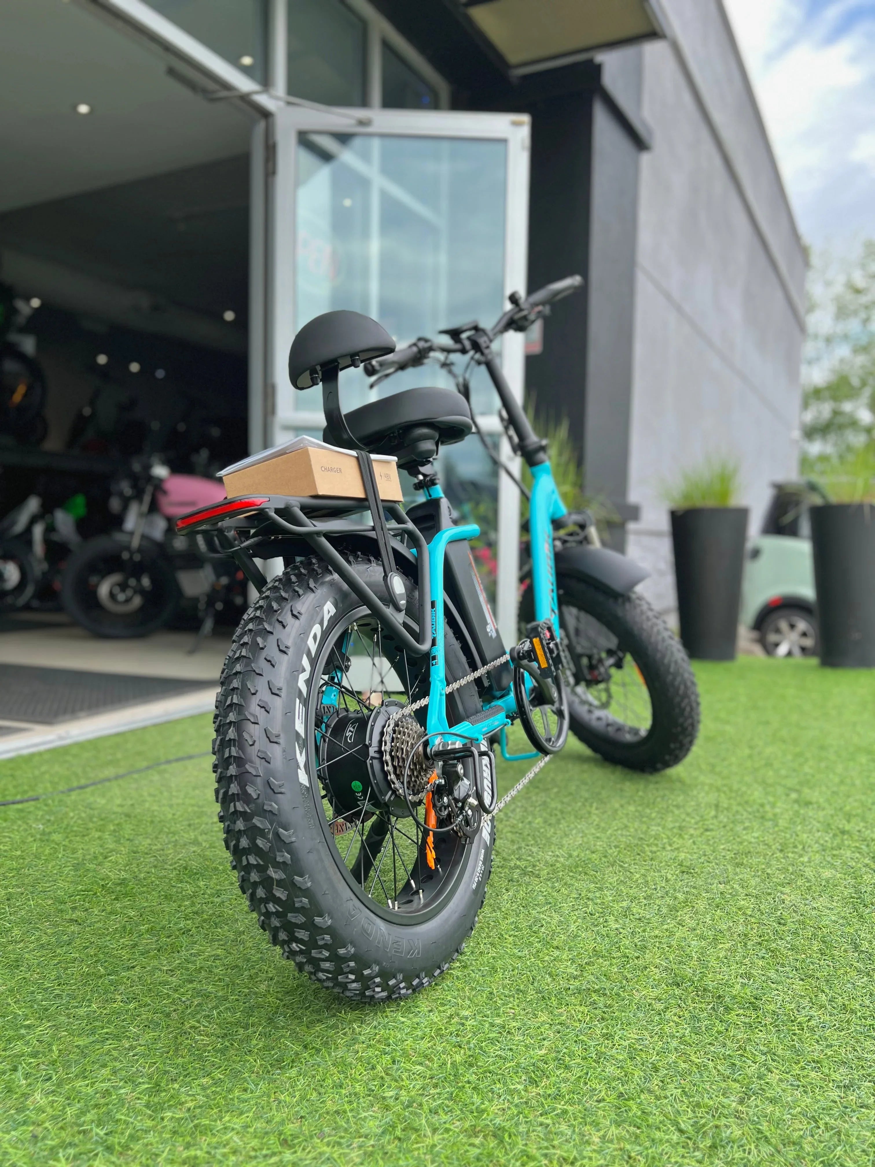 Blue fat tire electric bike with rear rack outside bike shop on artificial grass
