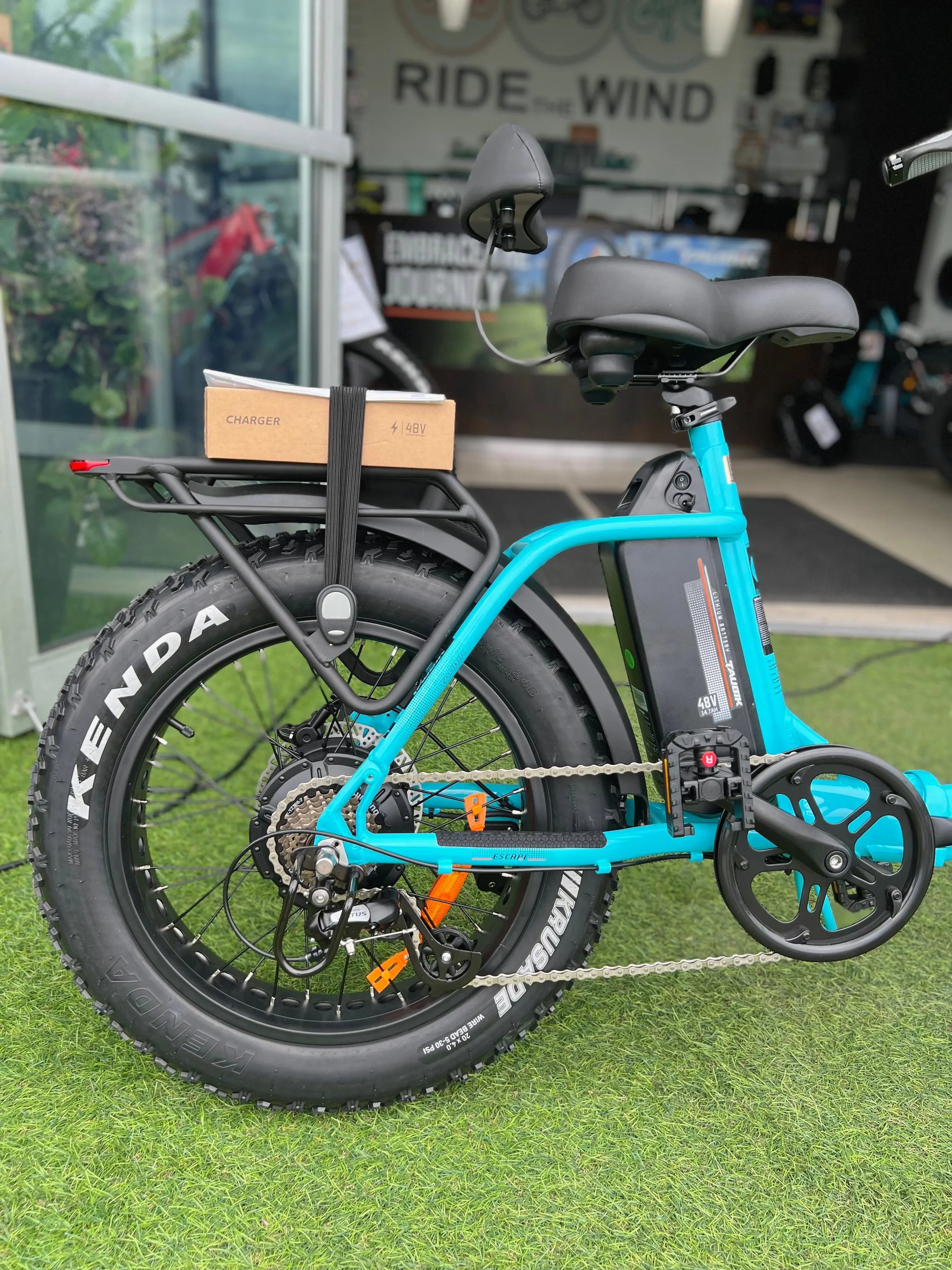 Blue electric bike with fat Kenda tires, 48V battery, and charger box on rear rack