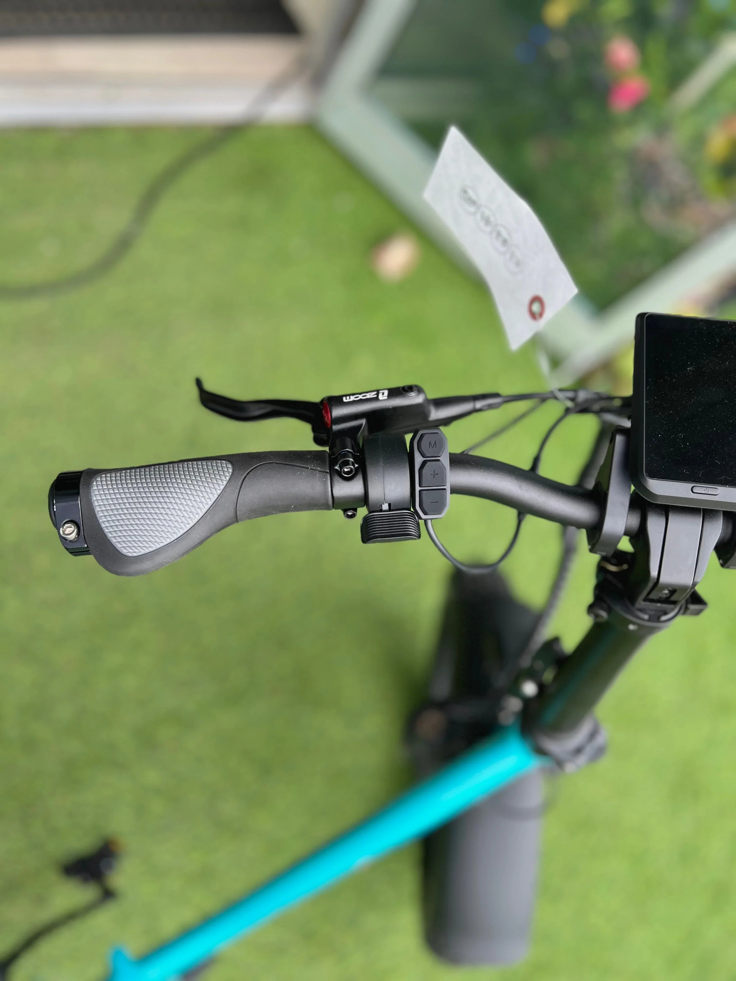 Close-up of electric scooter handlebar with brake lever, grip, and control buttons on green grass