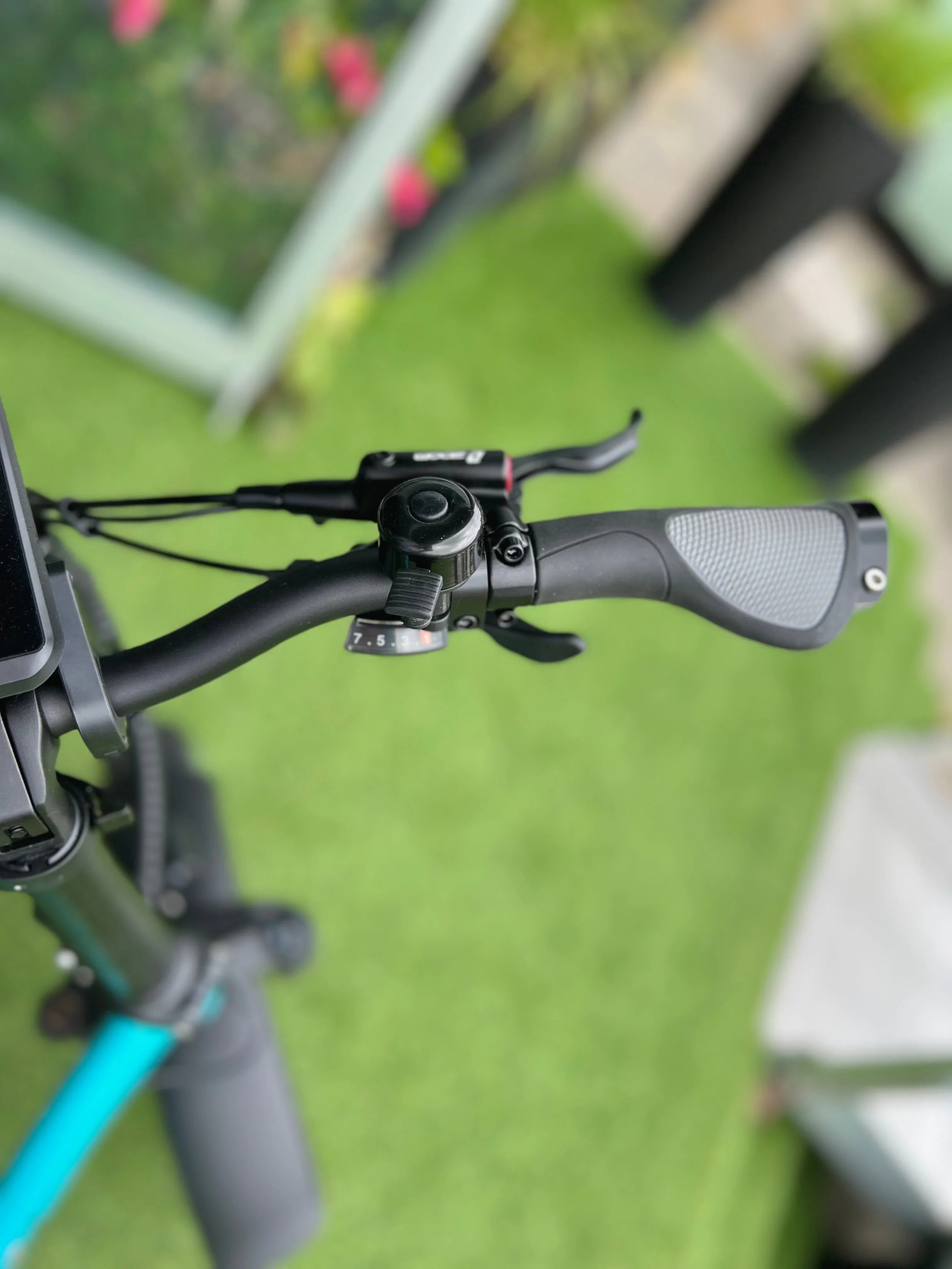 Close-up of black electric scooter handlebar with bell, grip, and gear indicator outdoors