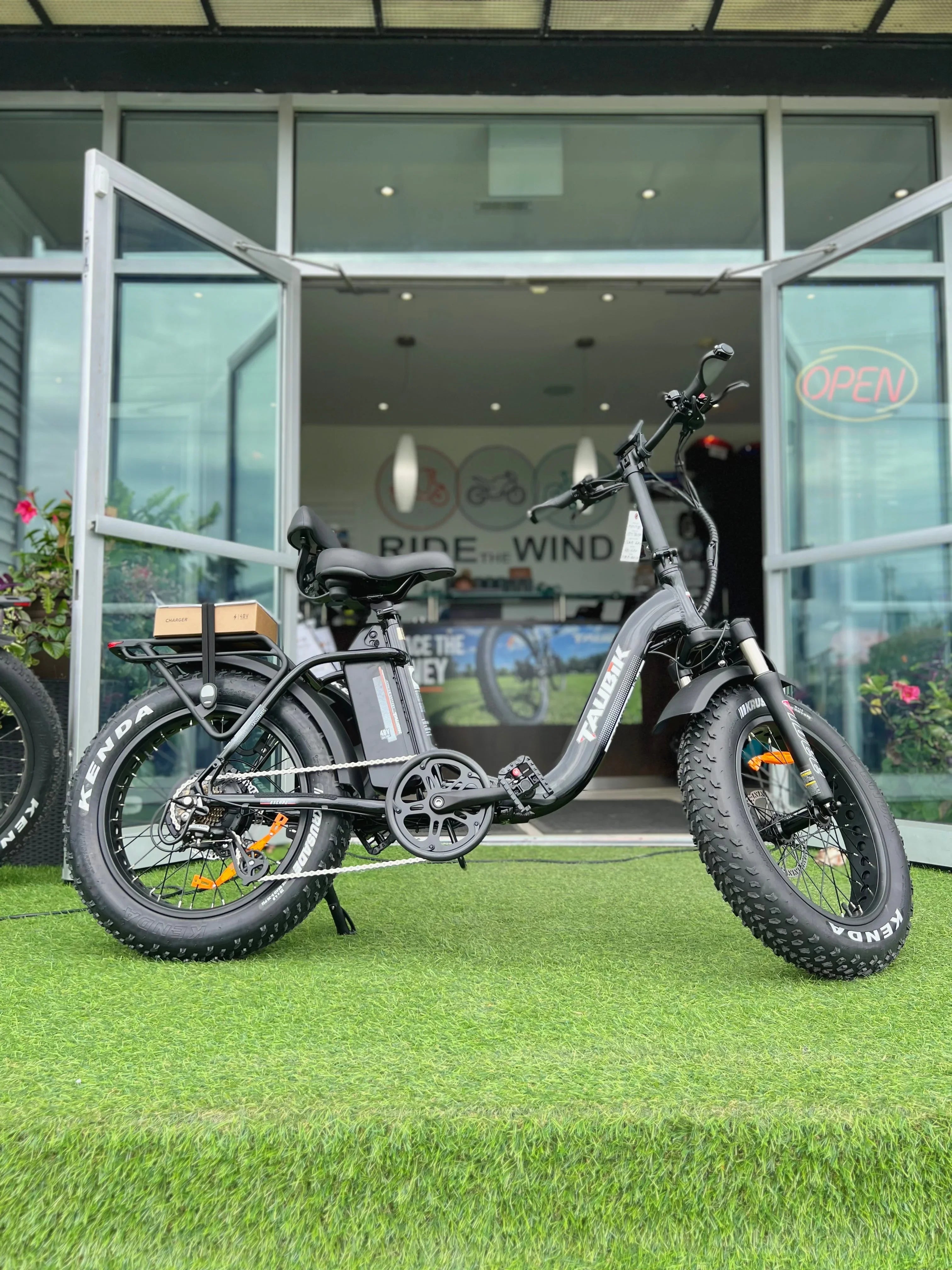 Fat tire electric bike TAURER on artificial grass outside bike shop with open glass doors