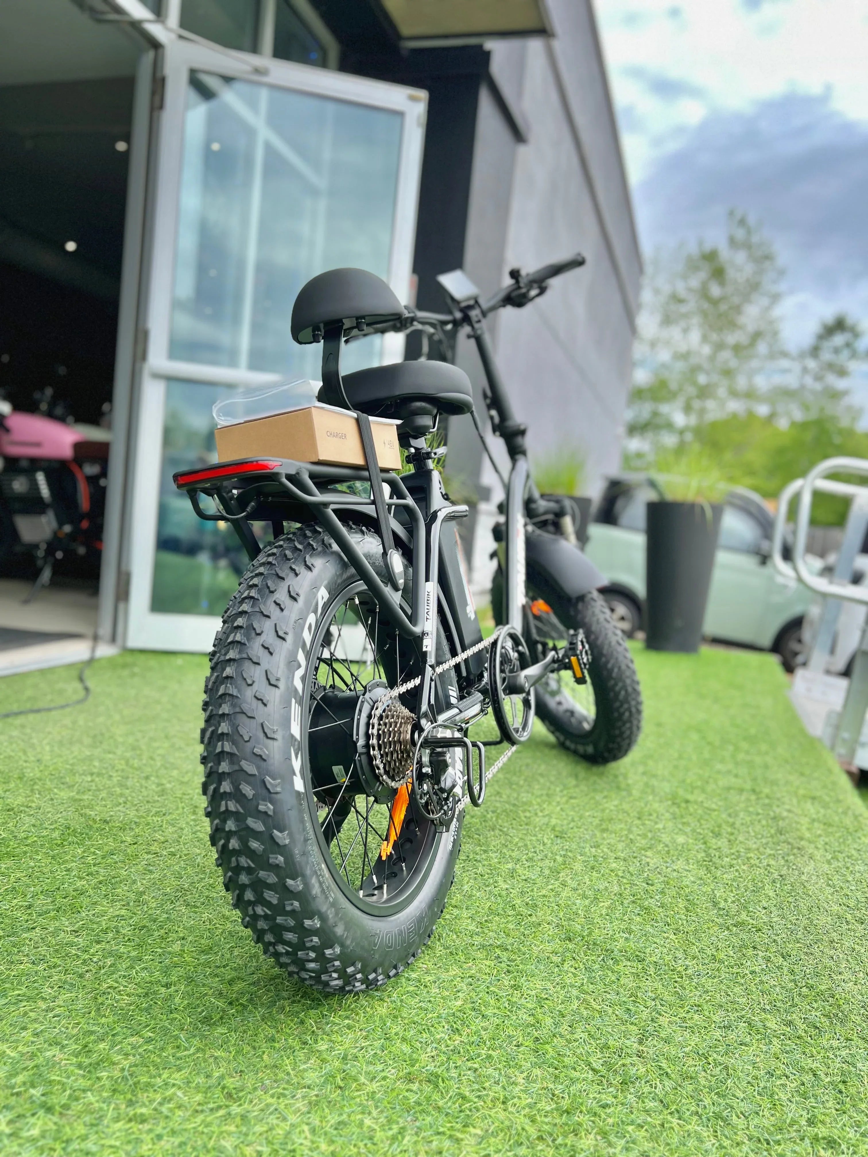 Fat tire electric bike with rear rack and charger box on artificial grass outside showroom