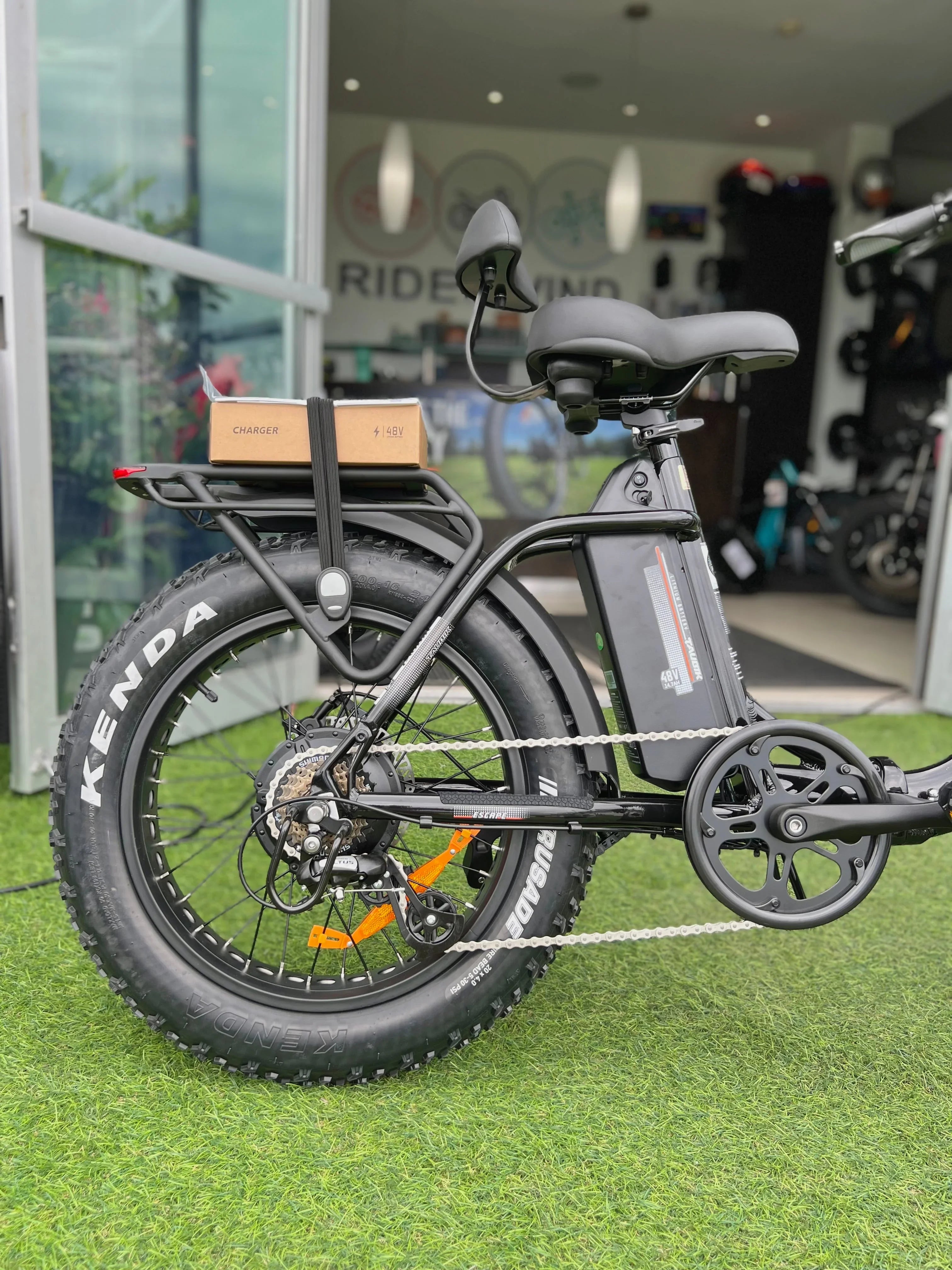 Fat tire electric bike with 48V battery and charger, parked on artificial grass outside shop