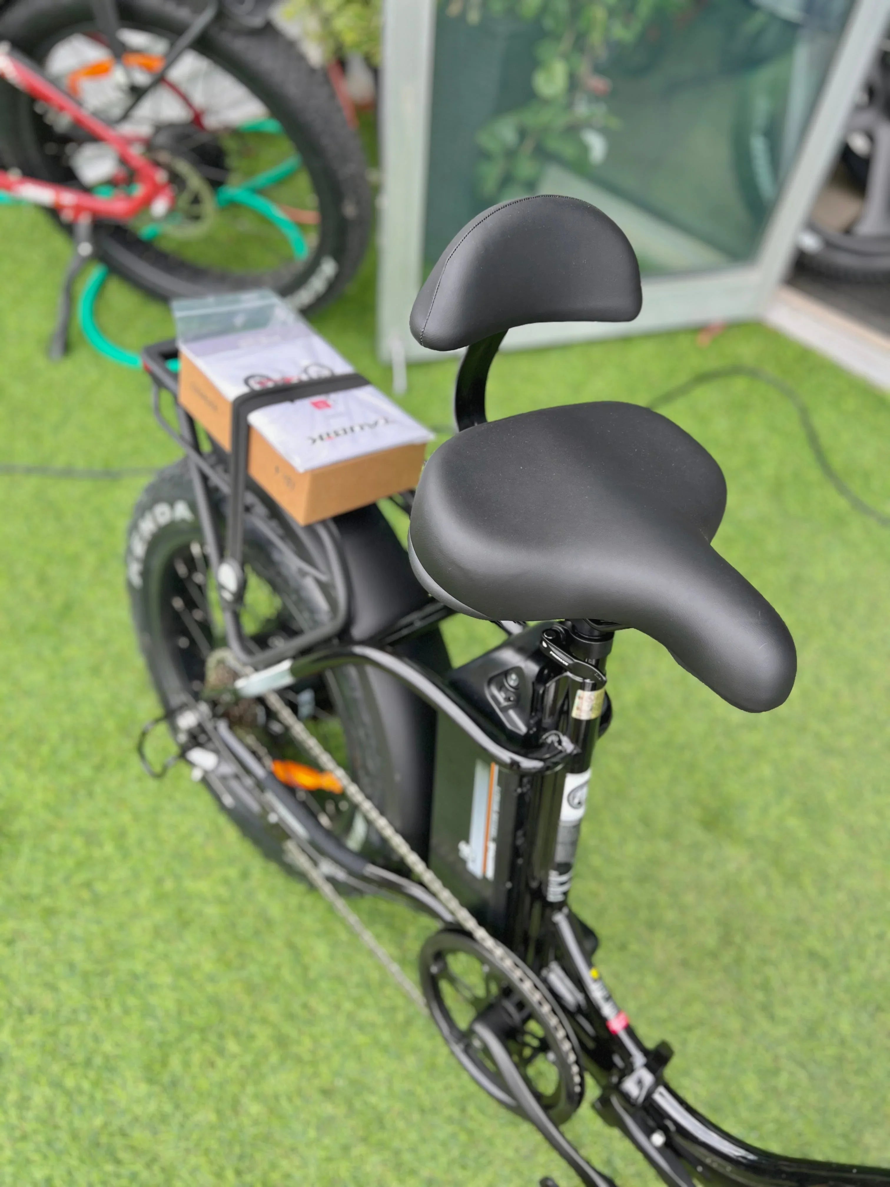 Black electric bike with backrest saddle and rear rack on green artificial grass