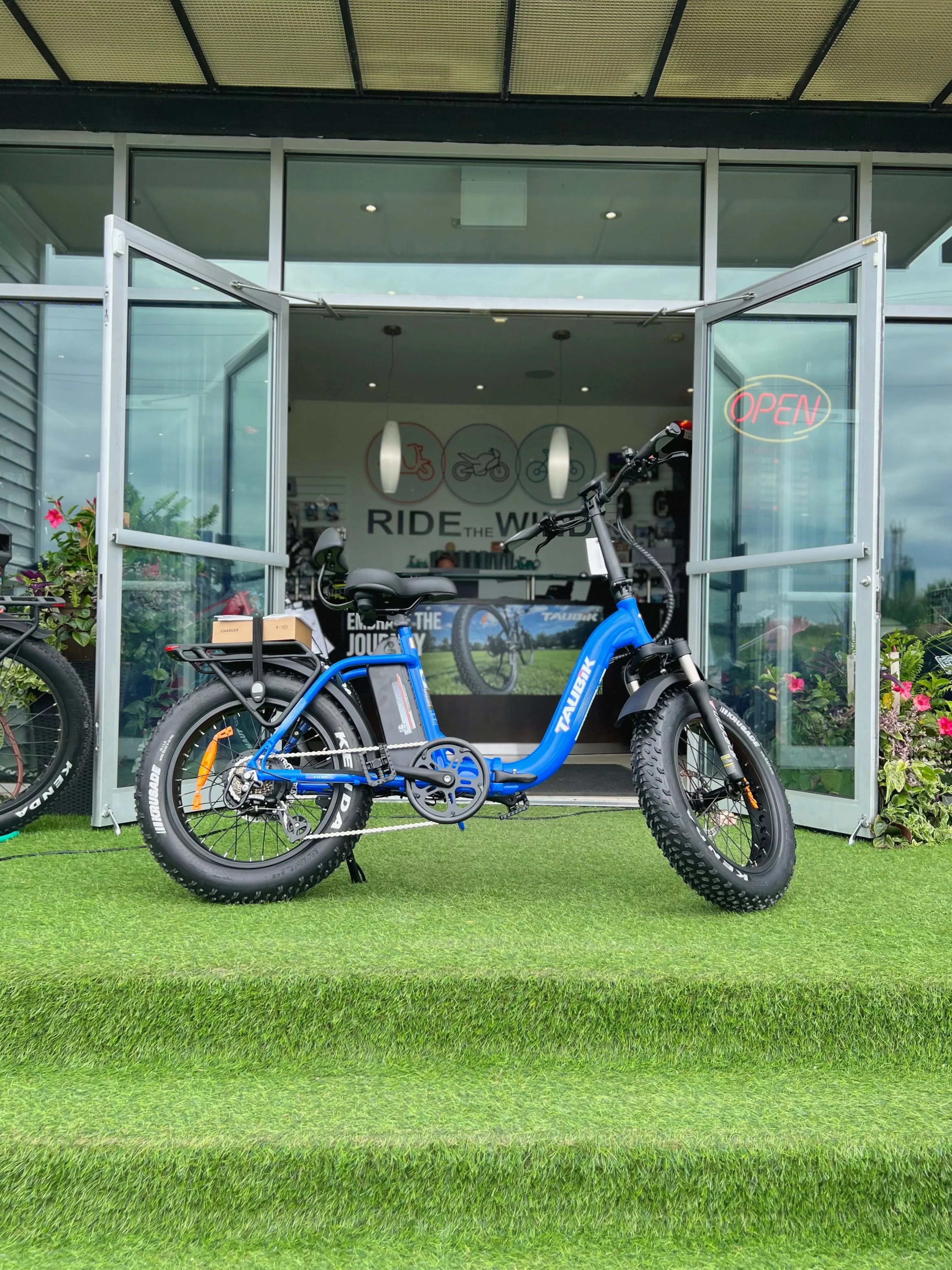 Blue fat tire electric bike parked outside bicycle shop with open glass doors