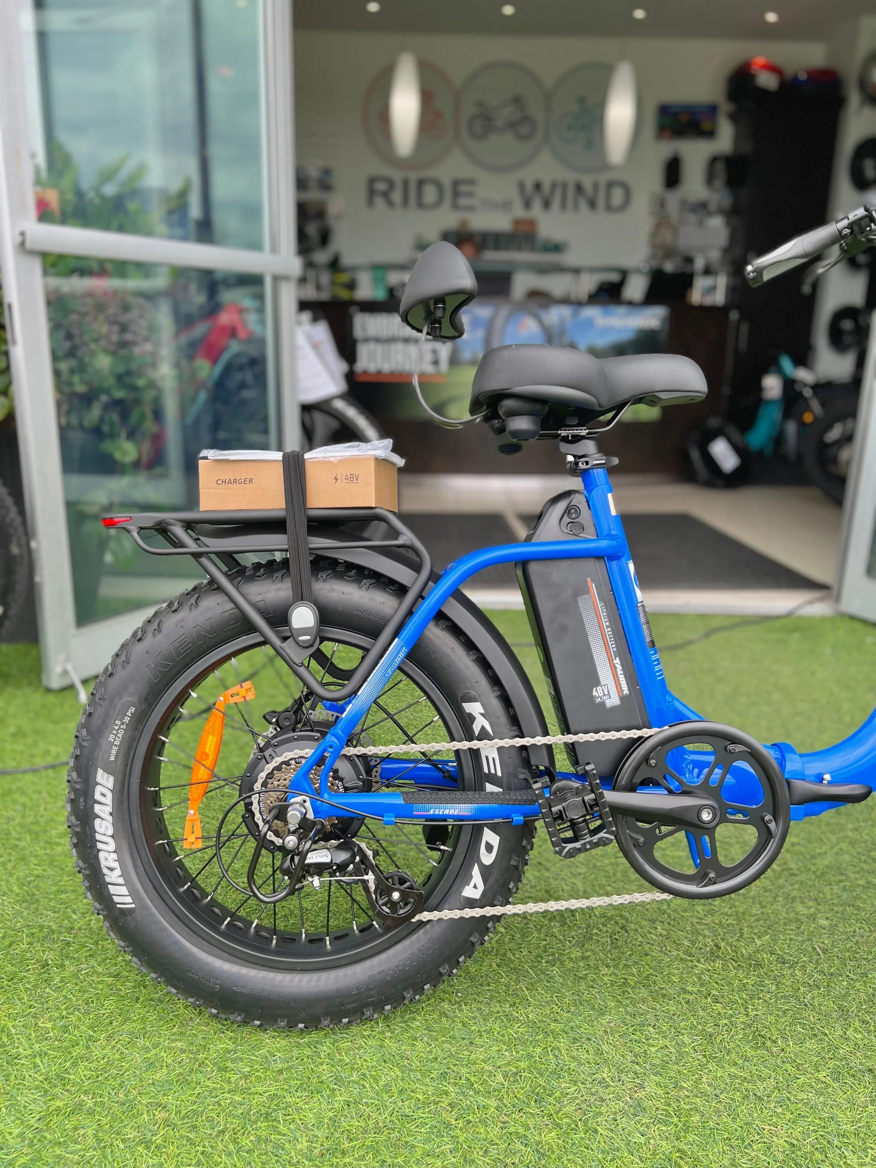 Blue fat tire electric bike with Kenda tires and charger, parked at Ride the Wind bike shop
