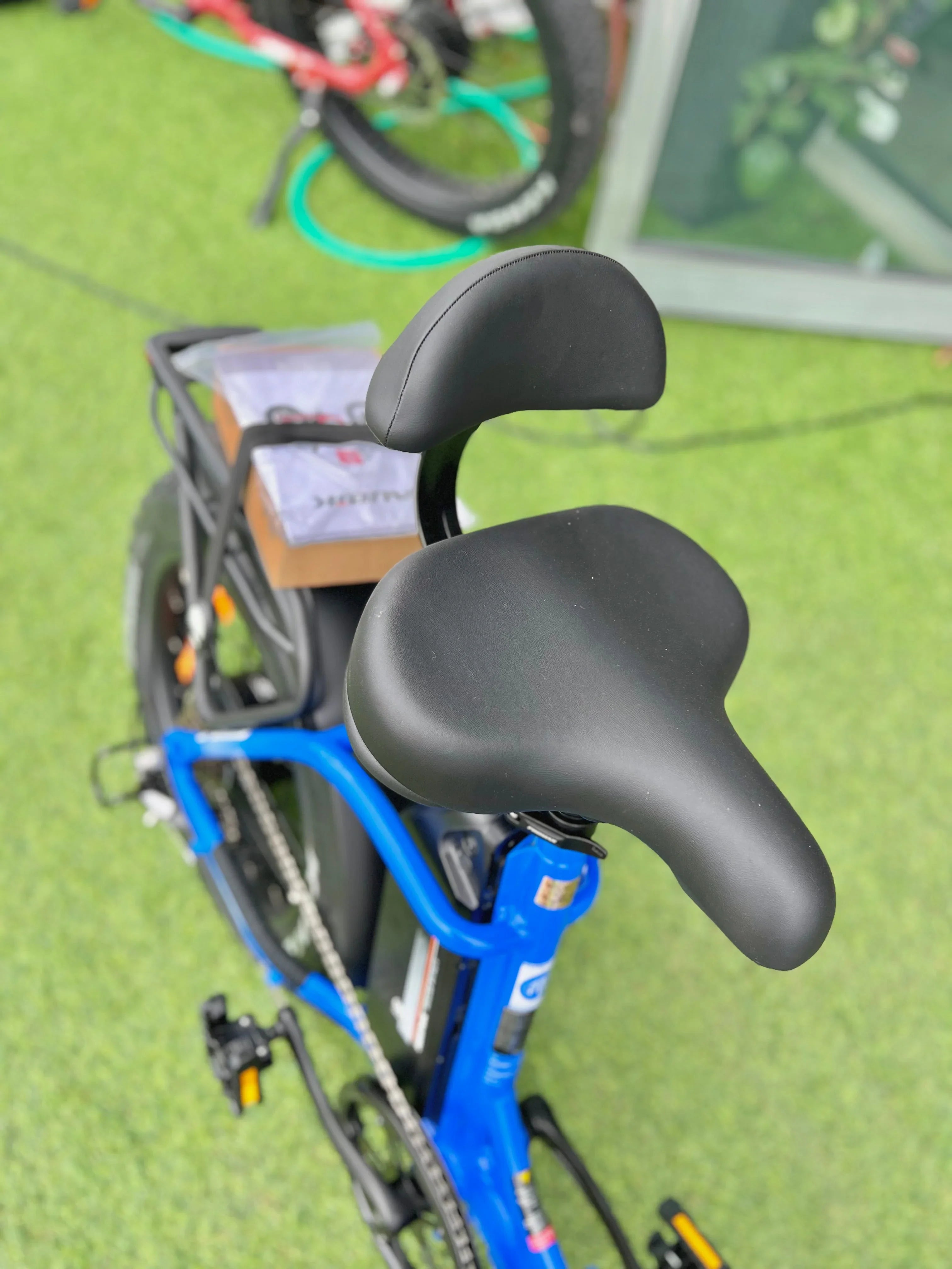 Blue electric bike with black cushioned seat and backrest, on green outdoor flooring