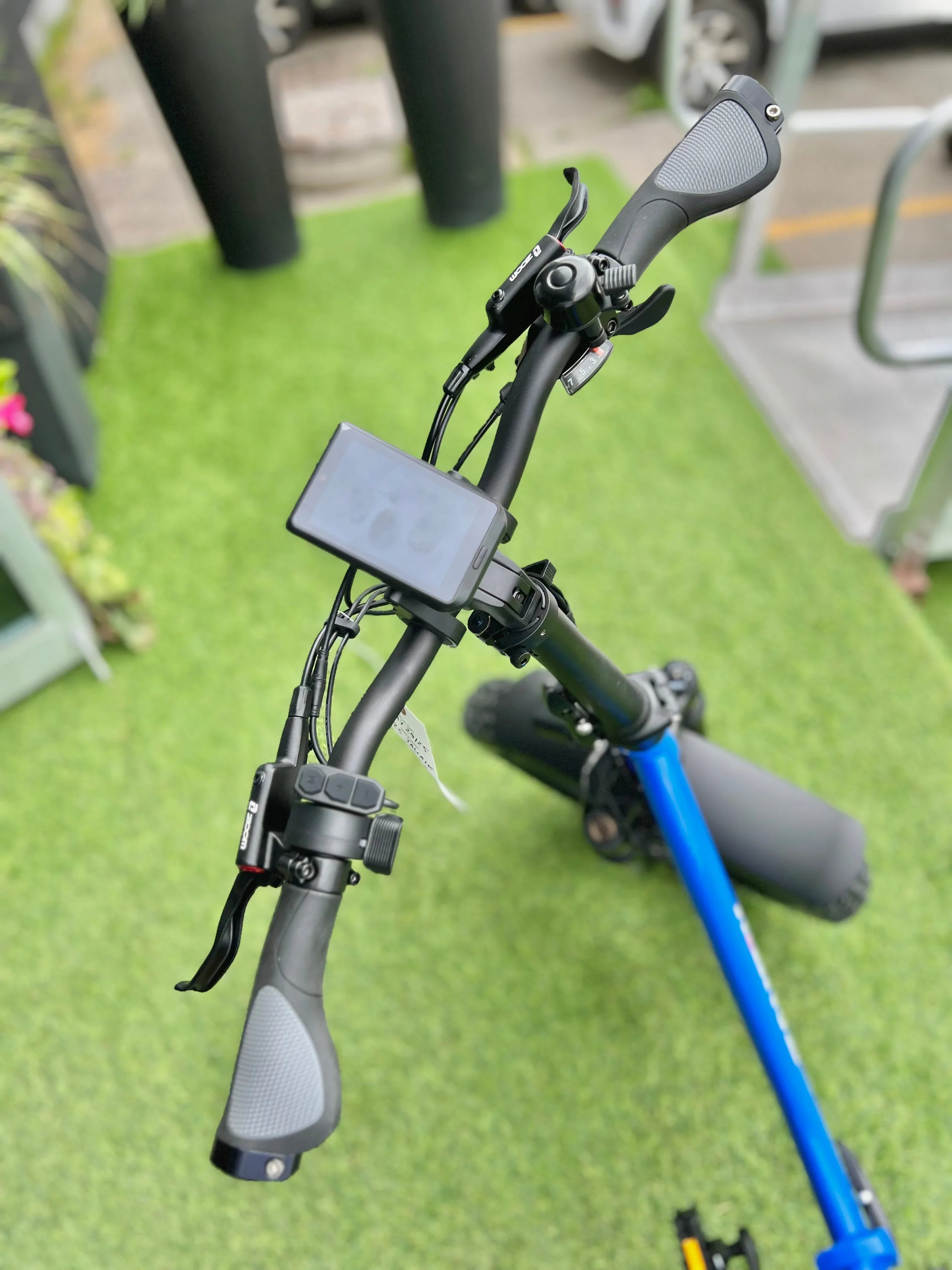 Close-up of electric scooter handlebars with display, controls, and bell on green grass