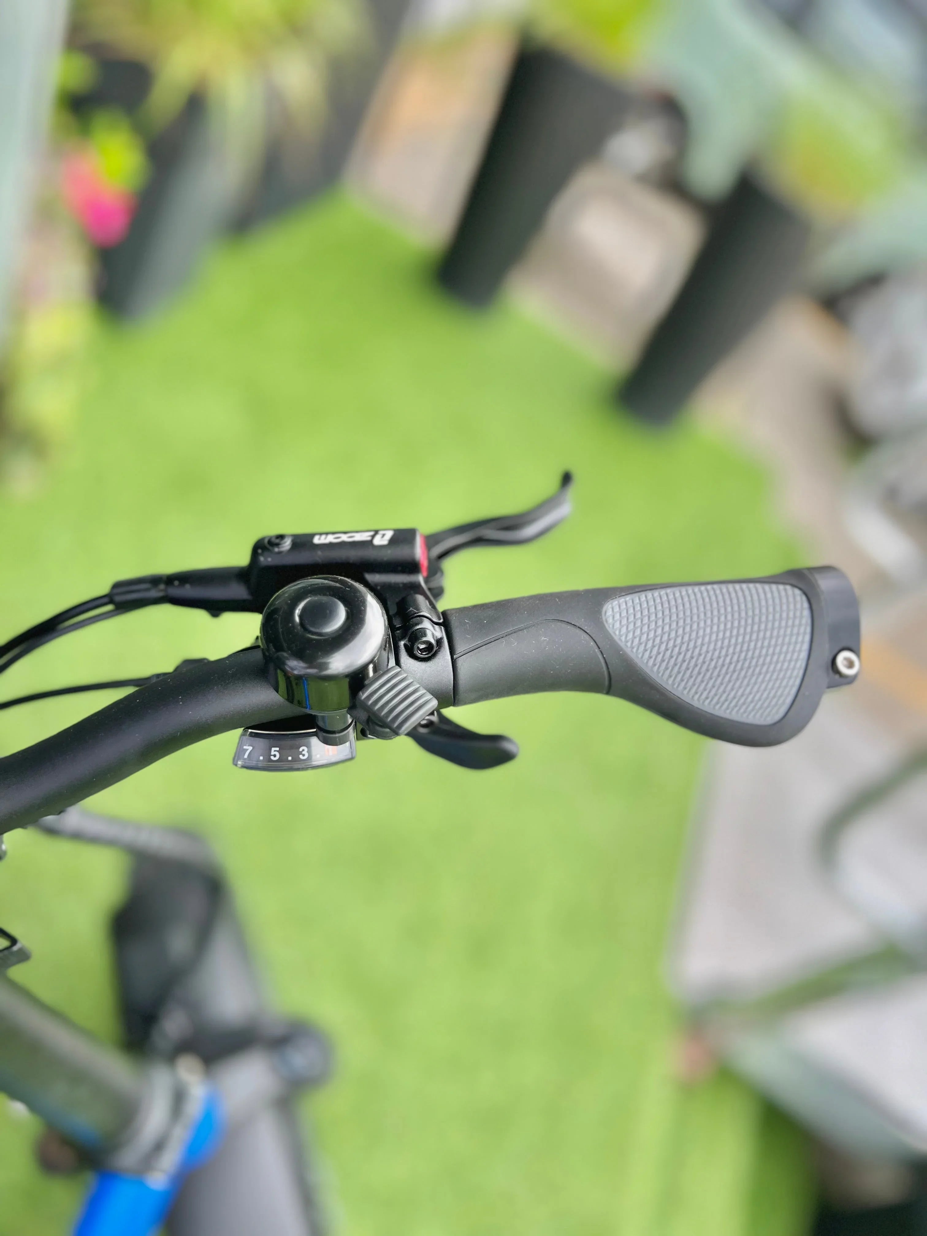 Close-up of a bicycle handlebar with gear shifter and ergonomic grip on green lawn