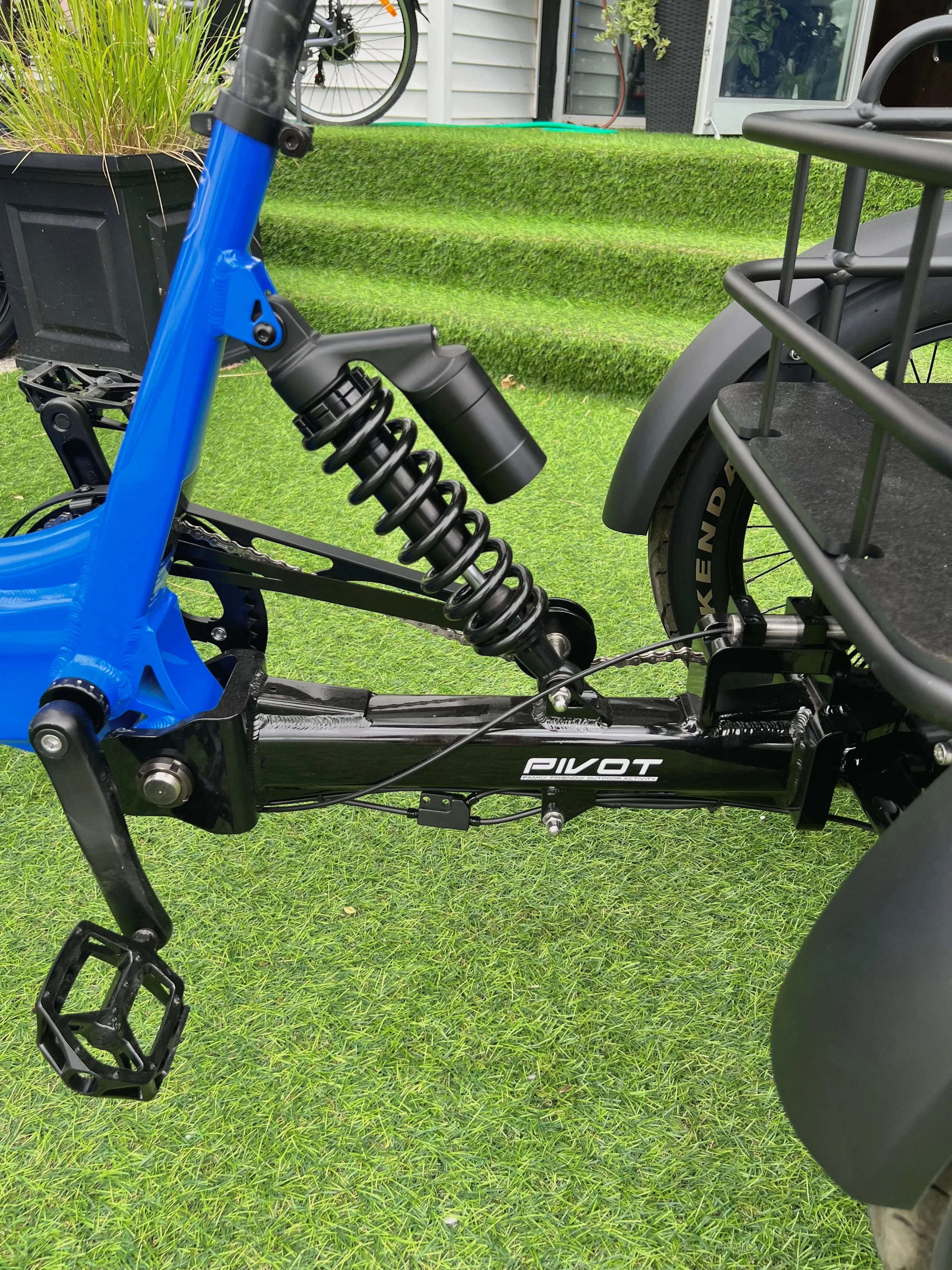 Close-up of blue electric bike rear suspension, pedal, and Pivot frame on artificial grass