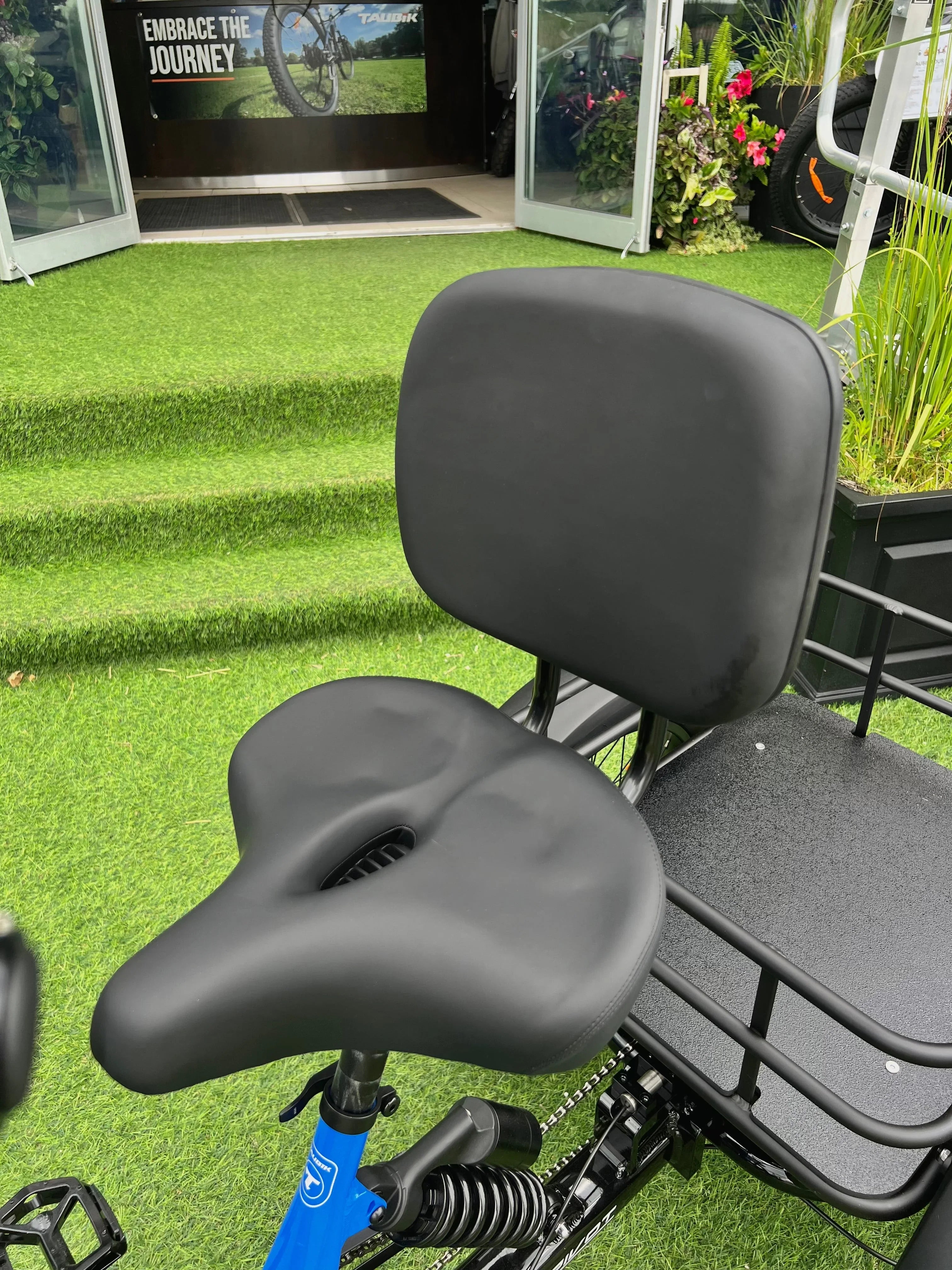 Comfortable bike seat with backrest on electric bike, showcased on artificial grass outside cycling shop